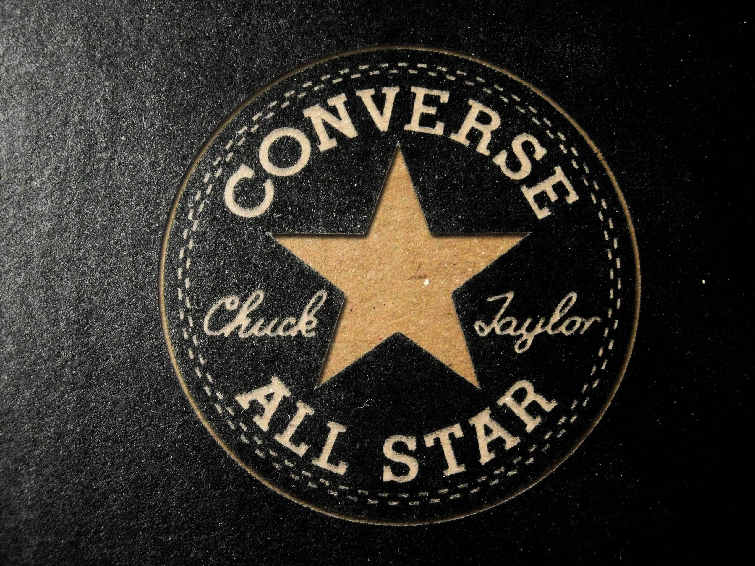 Converse Logo 桌布 壁紙 — 經典 Converse All Star 標誌布章的近距離特寫，在帶有紋理的黑色布料上，有米色星星和縫線。