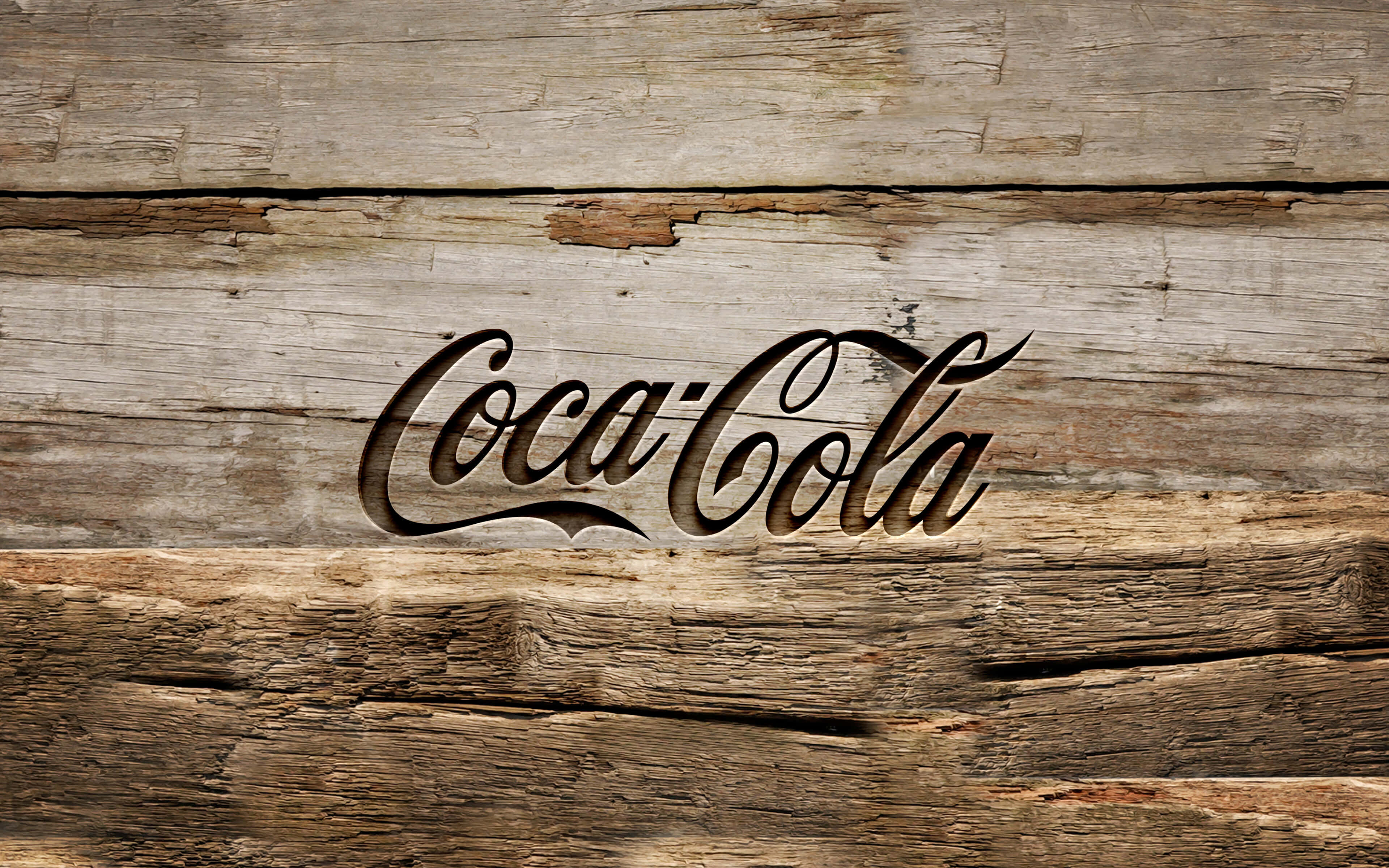 coca cola 桌布 壁紙 — 經典可口可樂草書標誌雕刻在風化的鄉村木板上，帶有天然木紋和質感。