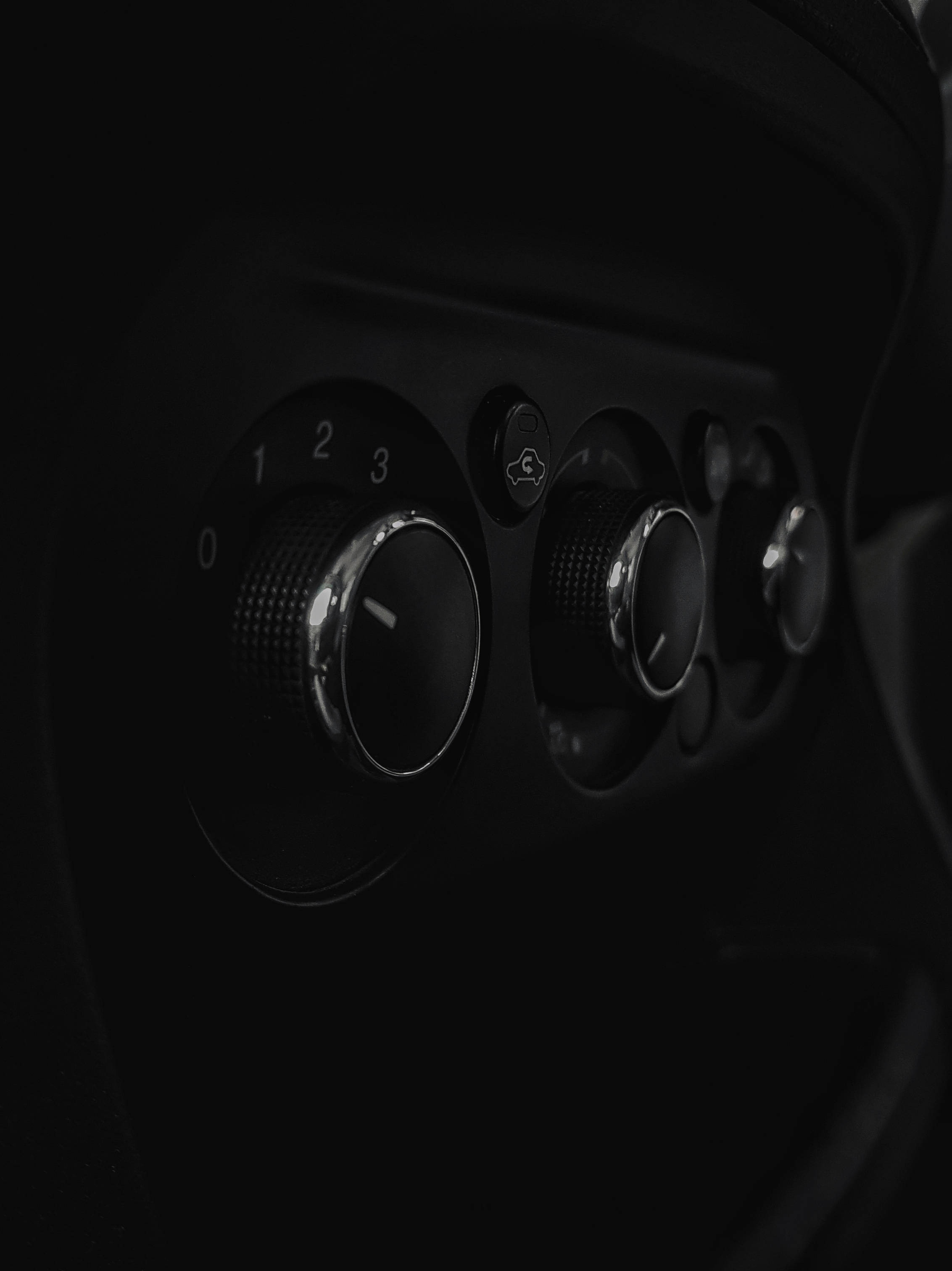 ford iPhone 桌布 壁紙 — 經典汽車空調控制旋鈕的特寫，在深色陰影中散發微光，帶有金屬光澤。