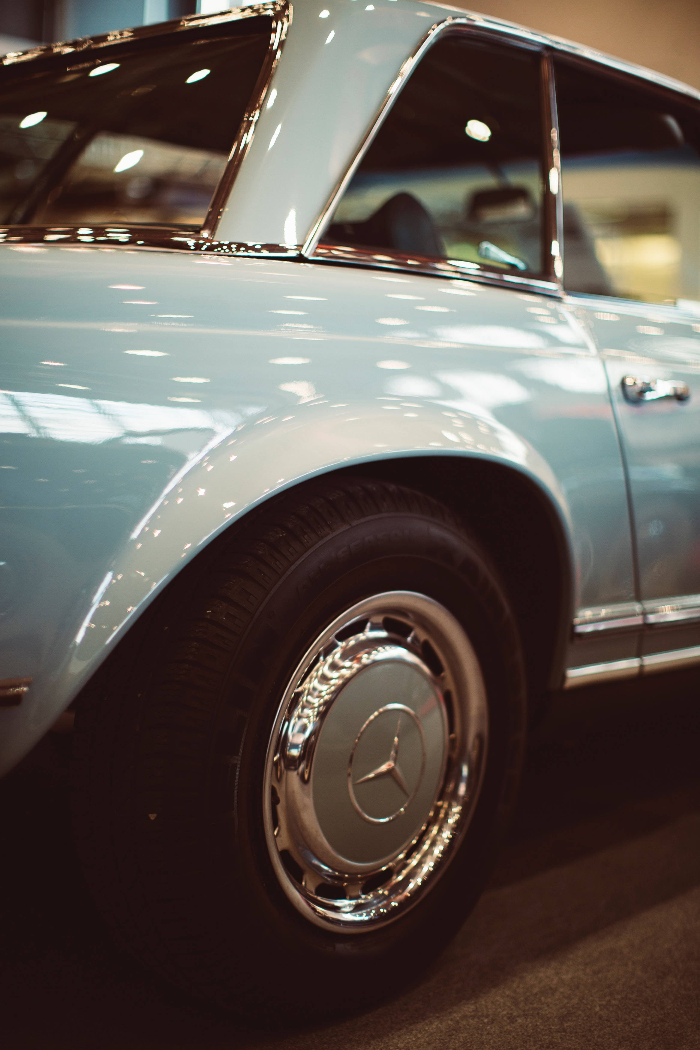 Retro 桌布 壁紙 — 經典淺藍色 Mercedes-Benz 汽車的特寫，展示其鍍鉻輪圈和流線型車身，在溫暖的室內燈光下。