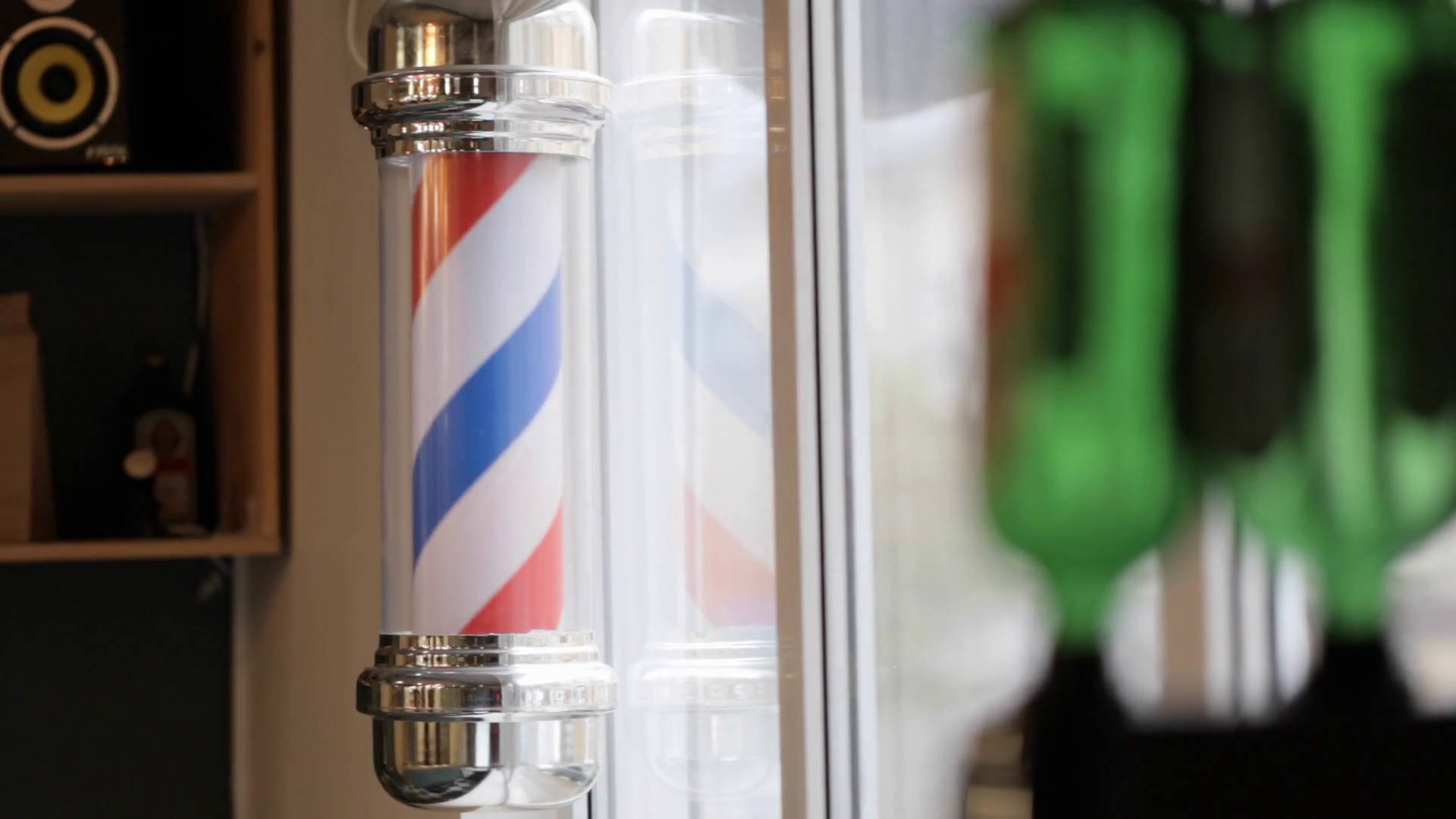 Barber 桌布 壁紙 — 經典理髮店紅白藍斜紋柱，焦點落在窗邊，背景有模糊的綠色瓶子。