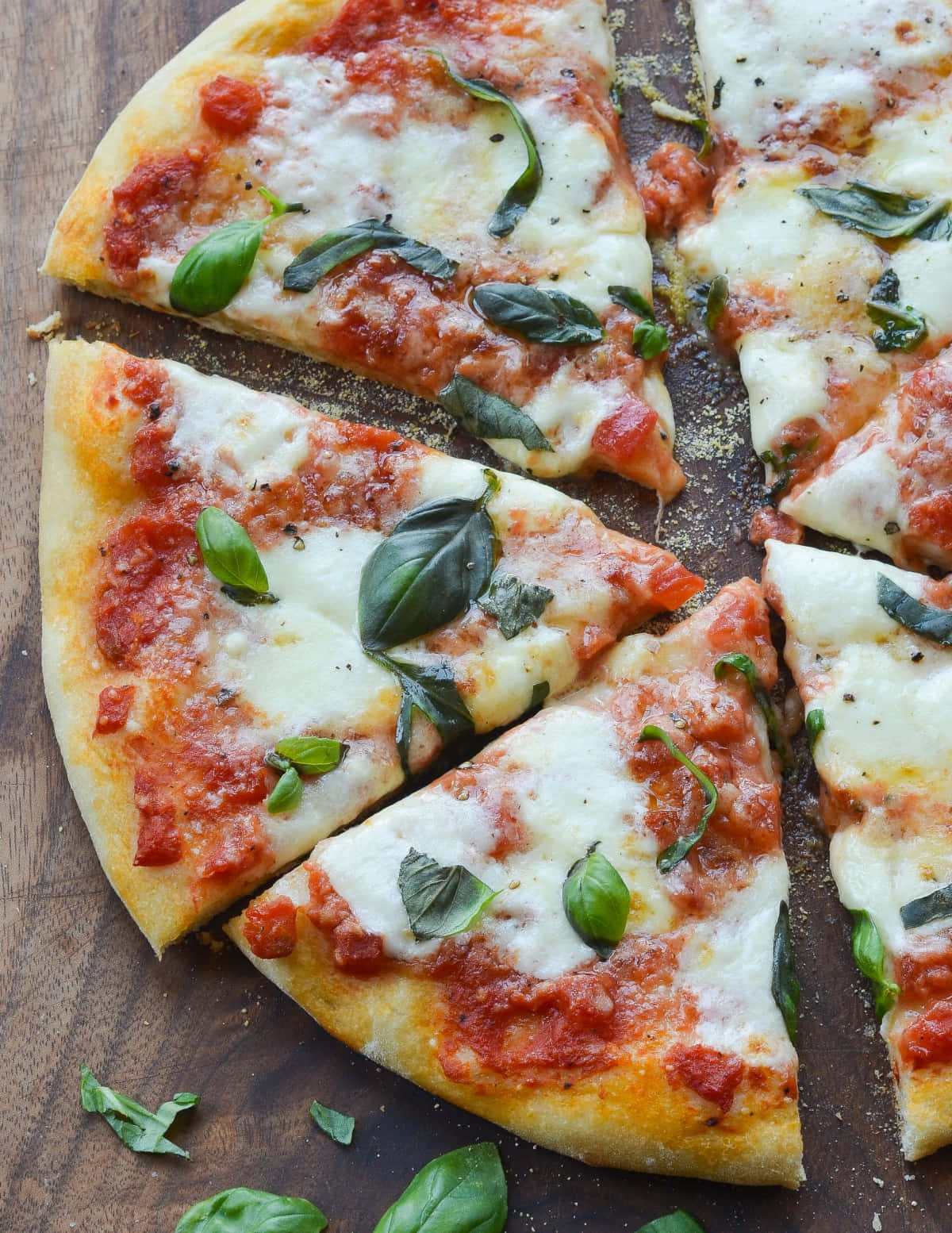 Pizza 桌布 壁紙 — 經典瑪格麗特披薩片，配上融化起司、番茄醬和新鮮羅勒，放在質樸的木板上。
