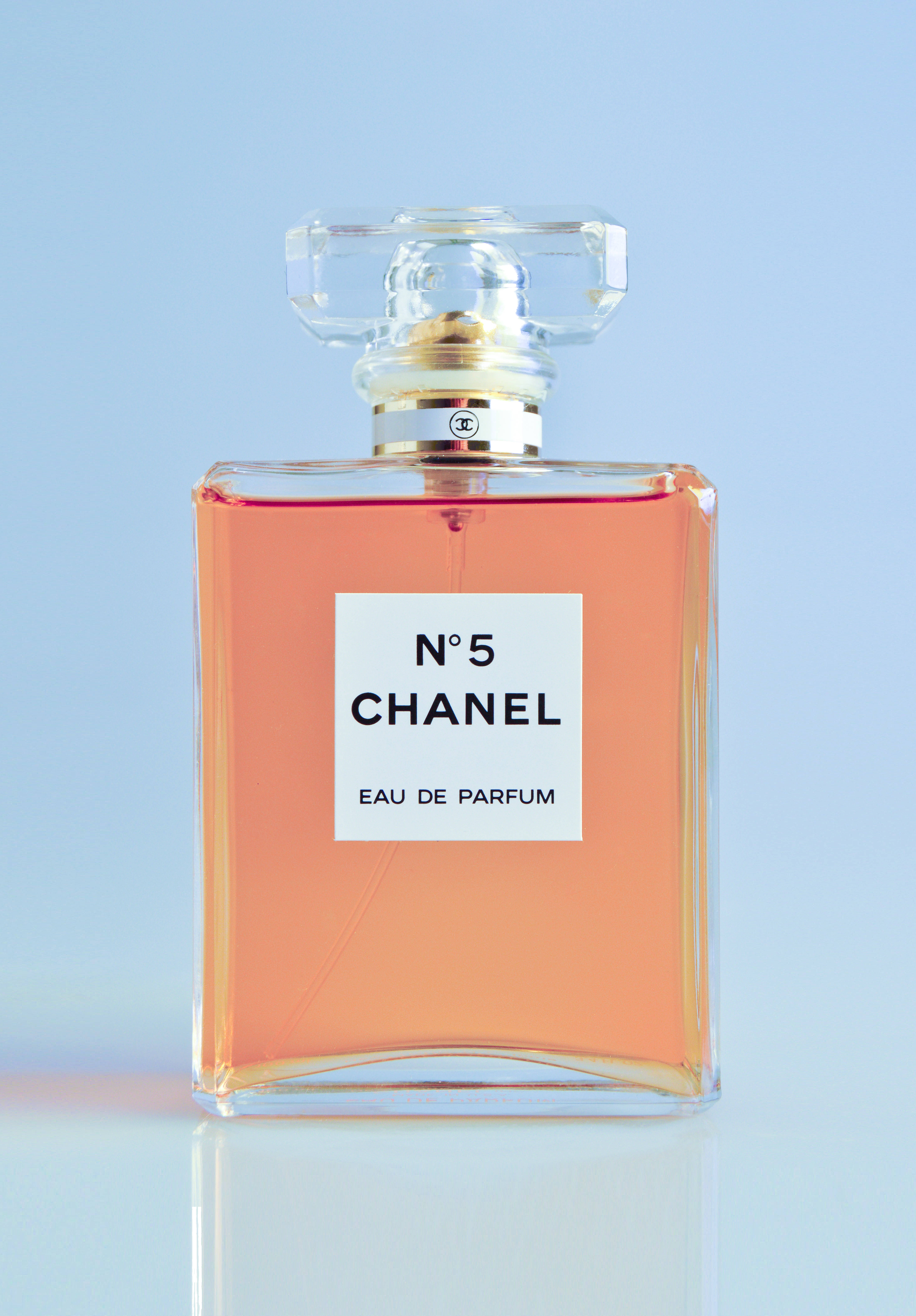 chanel iman 桌布 壁紙 — 經典的 Chanel No 5 香水瓶，裝有桃色液體，置於柔和的藍色背景中央。