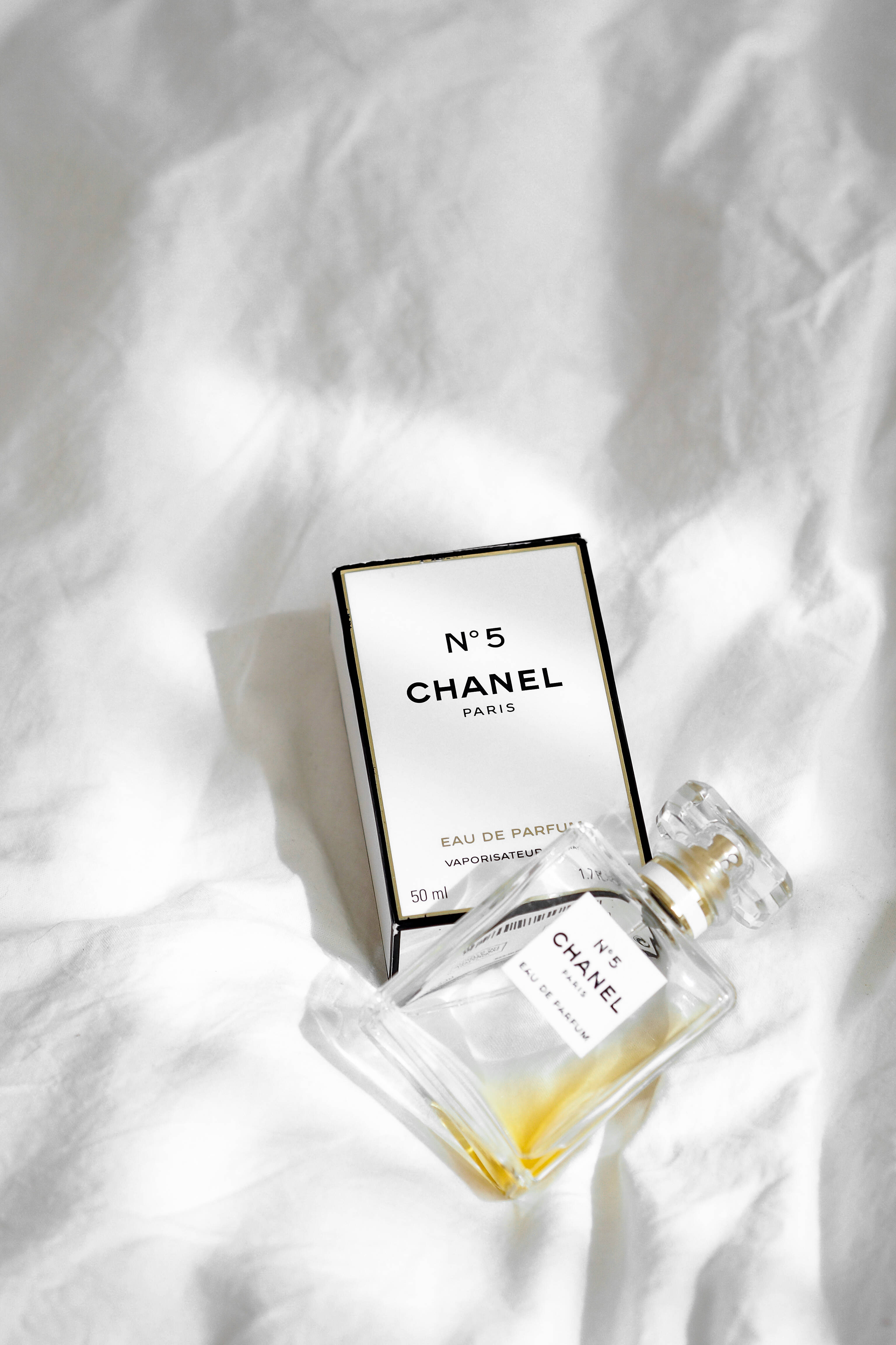 Chanel 桌布 壁紙 — 經典的 Chanel No 5 香水瓶和盒子優雅地放在柔軟的白色皺布上，在明亮的自然光下。