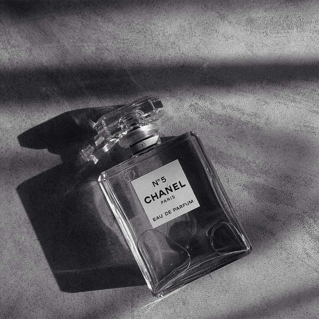 灰色 桌布 壁紙 — 經典的Chanel No 5香水瓶放在有紋理的布料上，呈現戲劇性的陰影效果。