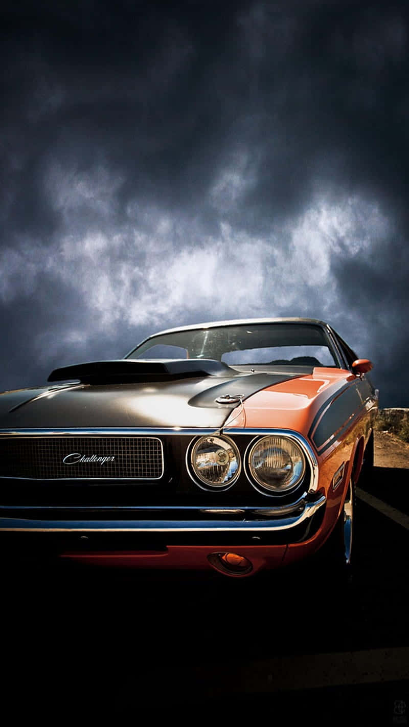 Dodge 桌布 壁紙 — 經典的橙色和黑色道奇挑戰者在黃昏時分戲劇性的暴風雲下閃閃發光。