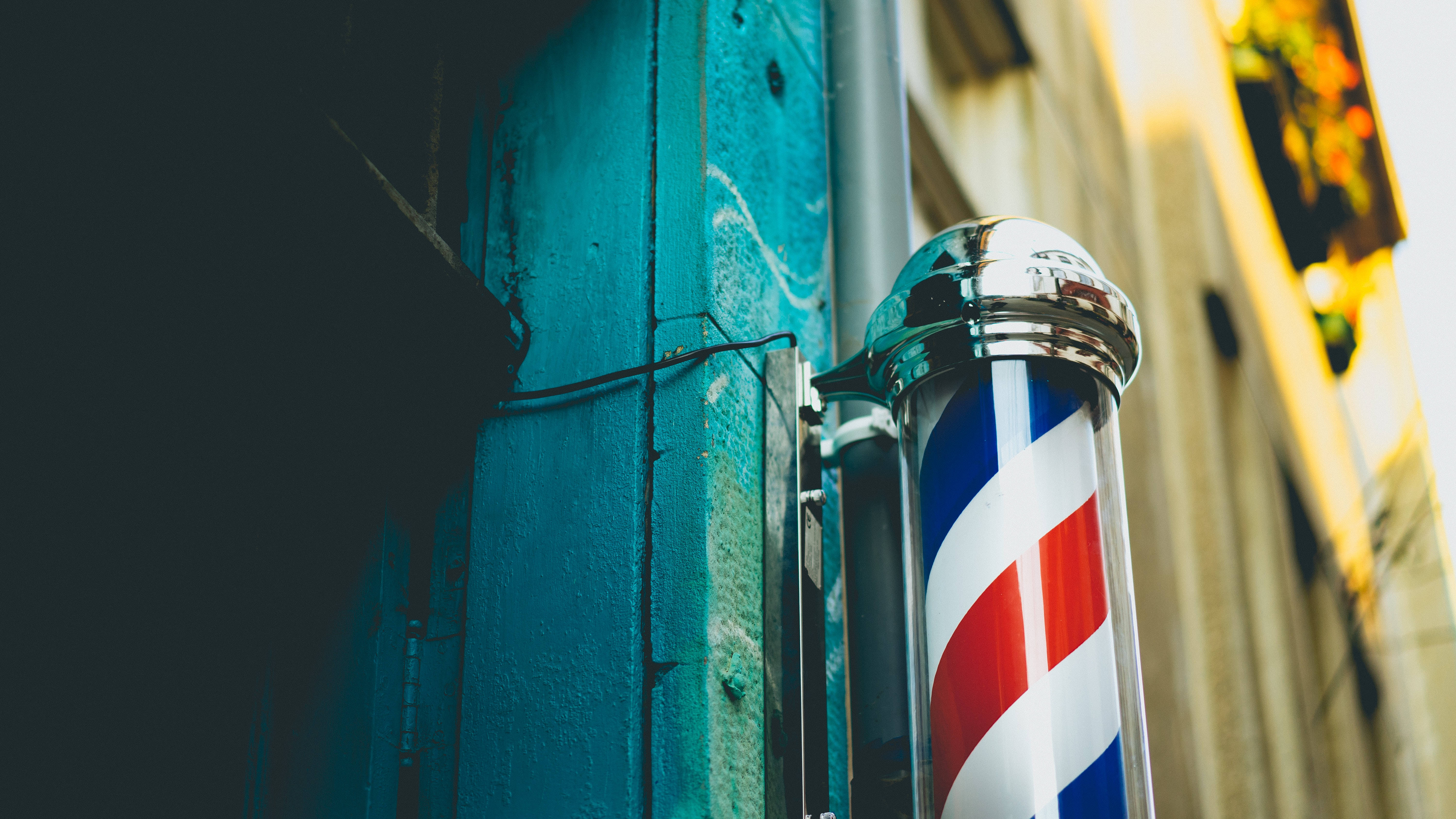 Barber 桌布 壁紙 — 經典的紅白藍理髮柱在溫暖的金色陽光下，在風化的青綠色牆壁上閃閃發光。