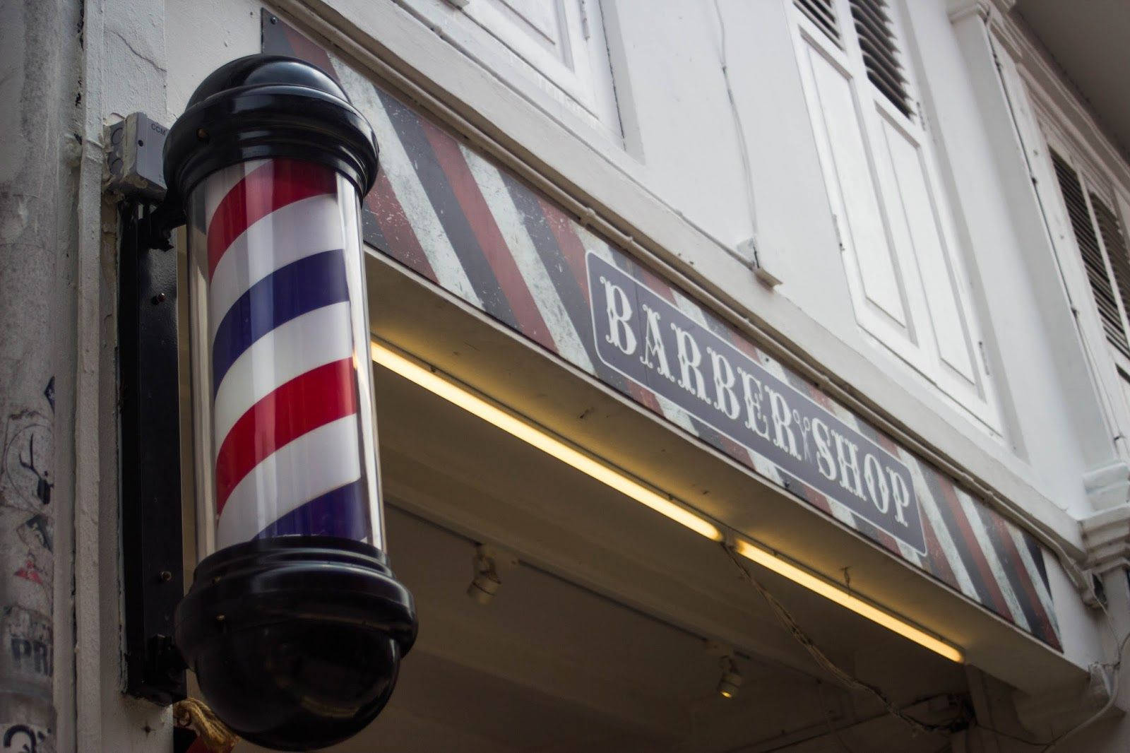 Barber 桌布 壁紙 — 經典的紅白藍理髮柱在溫暖的霓虹燈下，在一塊復古理髮店招牌旁邊閃閃發光。