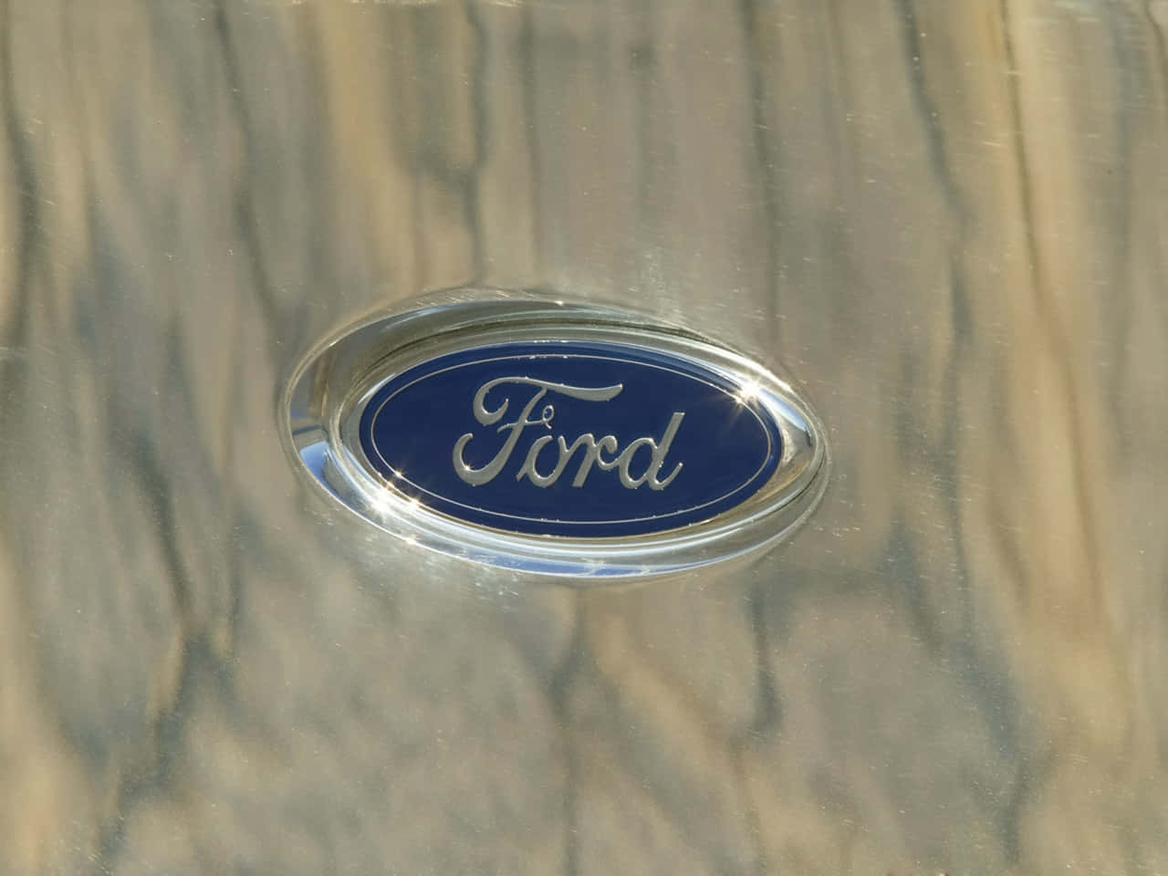 Ford Logo 桌布 壁紙 — 經典福特標誌在鍍鉻汽車表面上閃耀的特寫，帶有模糊的樹木倒影。