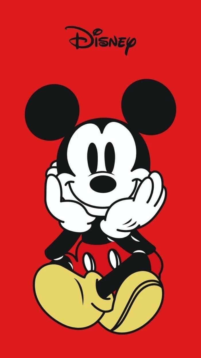 Mickey Mouse Home 桌布 壁紙 — 經典米奇老鼠穿著標誌性的紅色短褲和黃色鞋子，雙手緊握，在鮮紅色的背景前微笑坐著。