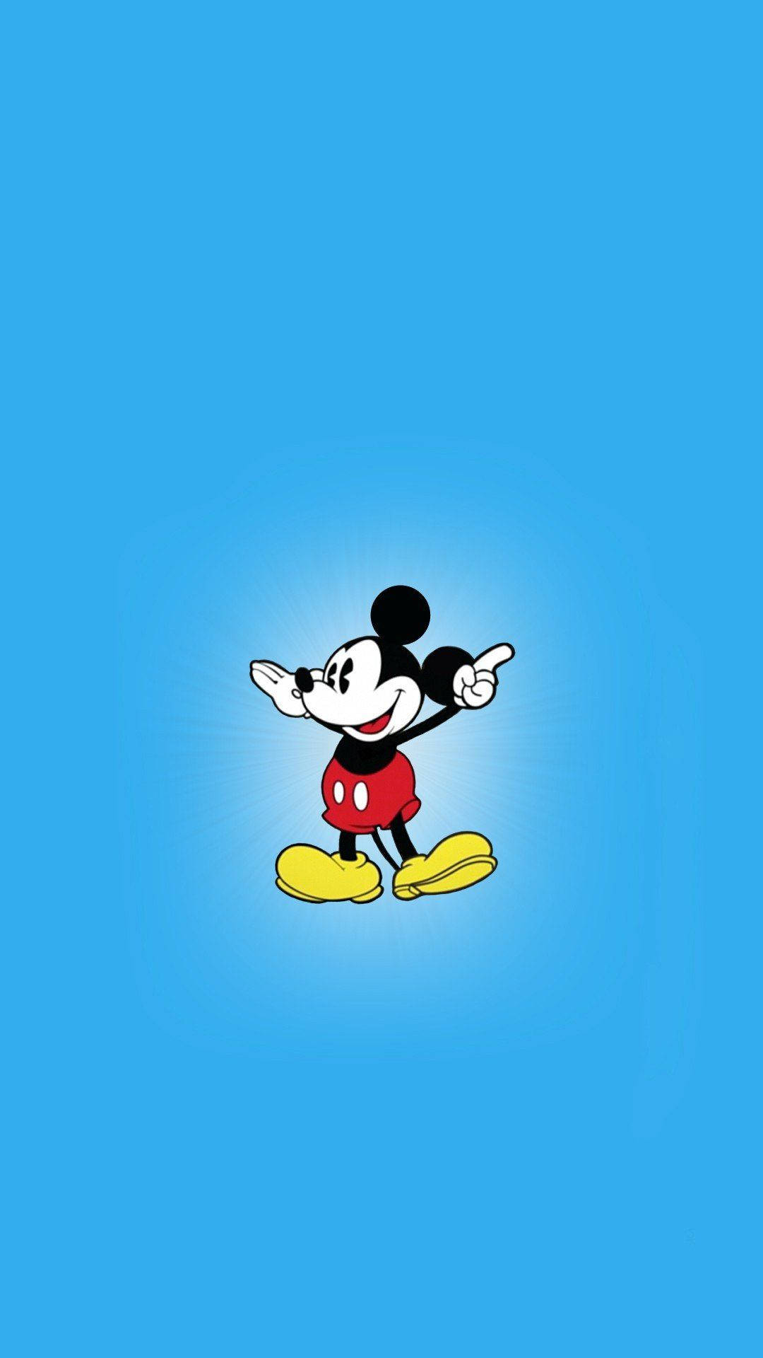 Mickey 桌布 壁紙 — 經典米奇老鼠穿著紅色短褲和黃色鞋子，在純藍色背景上帶著發光光環愉快地指著。