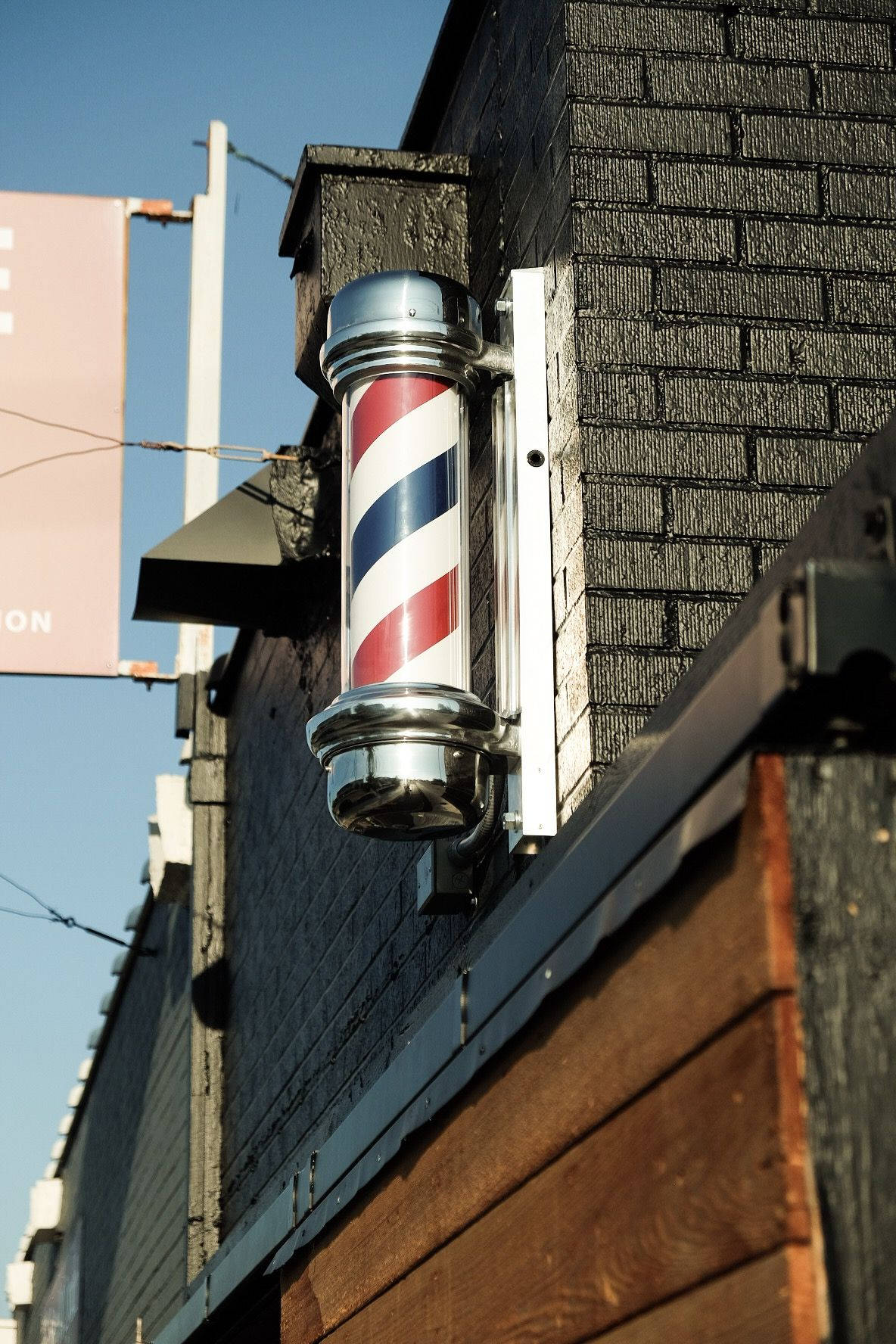 Barber 桌布 壁紙 — 經典紅白藍理髮柱安裝在深色磚砌建築上，背景是晴朗的藍天。