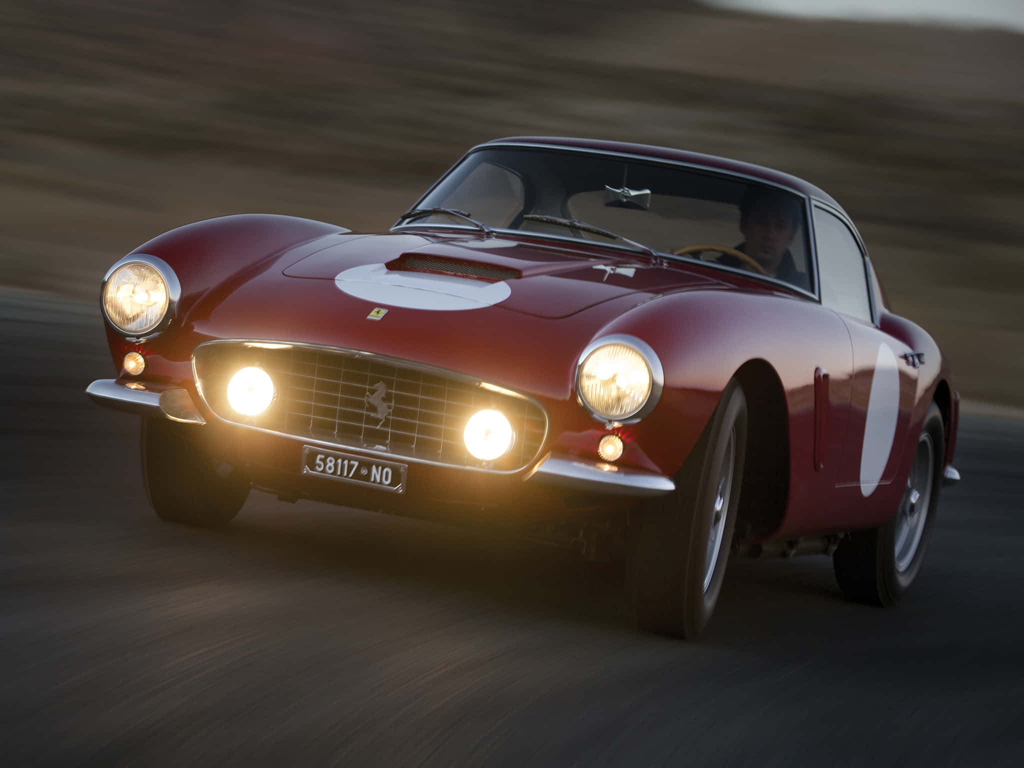 Vintage Ferrari 桌布 壁紙 — 經典紅色法拉利向前飛馳，閃爍的車頭燈在金色光線下劃過模糊的瀝青路面。