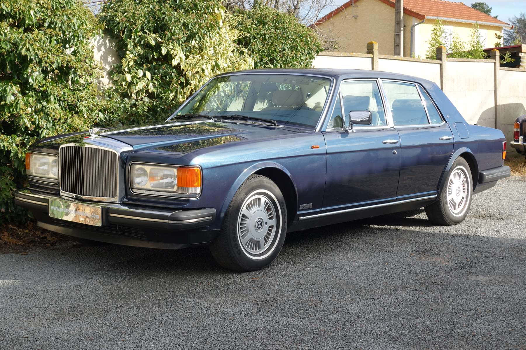 Bentley Eight 桌布 壁紙 — 經典藍色賓利轎車在明亮日光下停泊在碎石上，旁邊有綠色灌木叢。