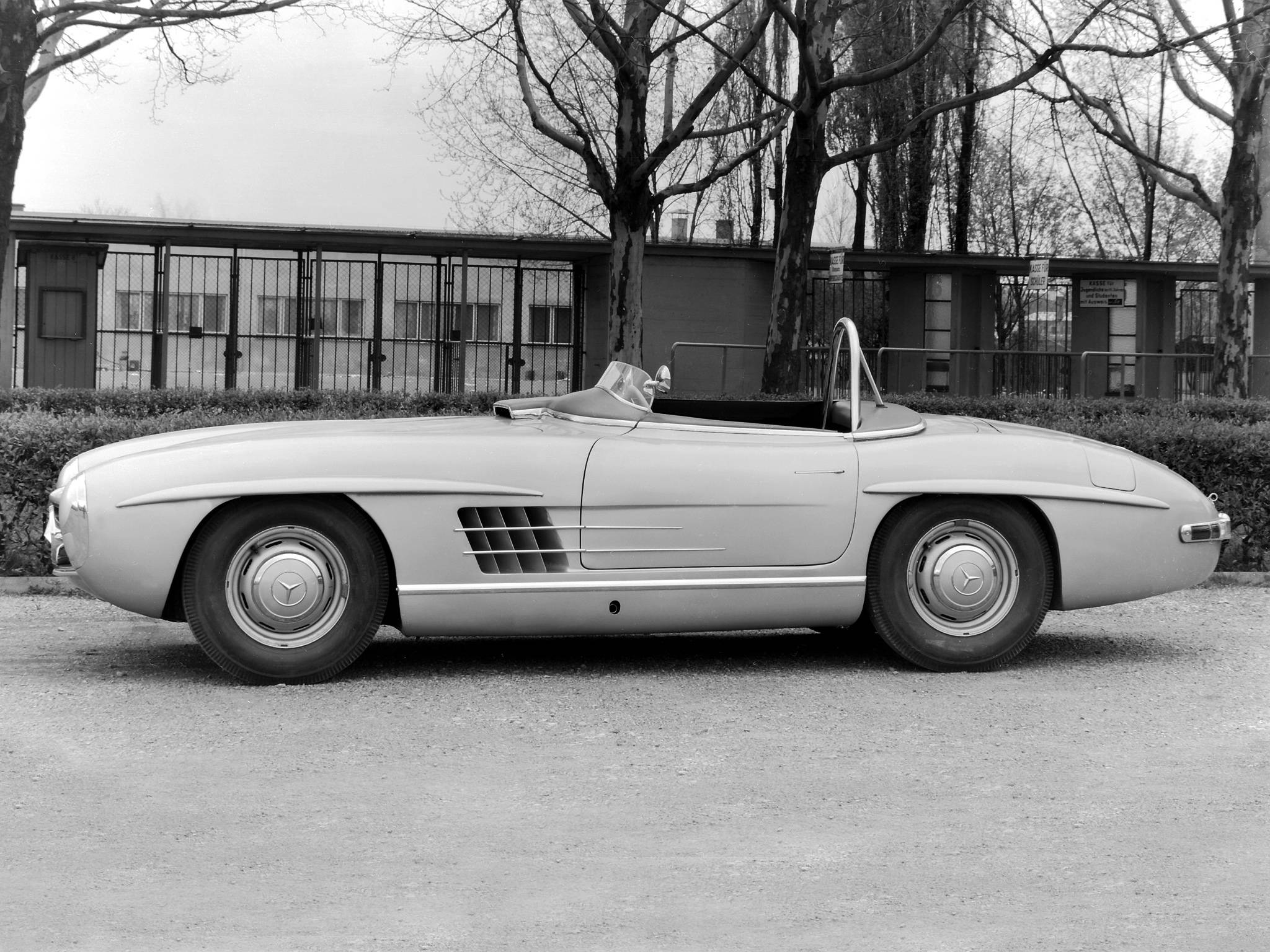 HD mercedes 桌布 壁紙 — 經典銀色賓士300SL鷗翼停泊在碎石上，背景有光禿的樹木和建築物。