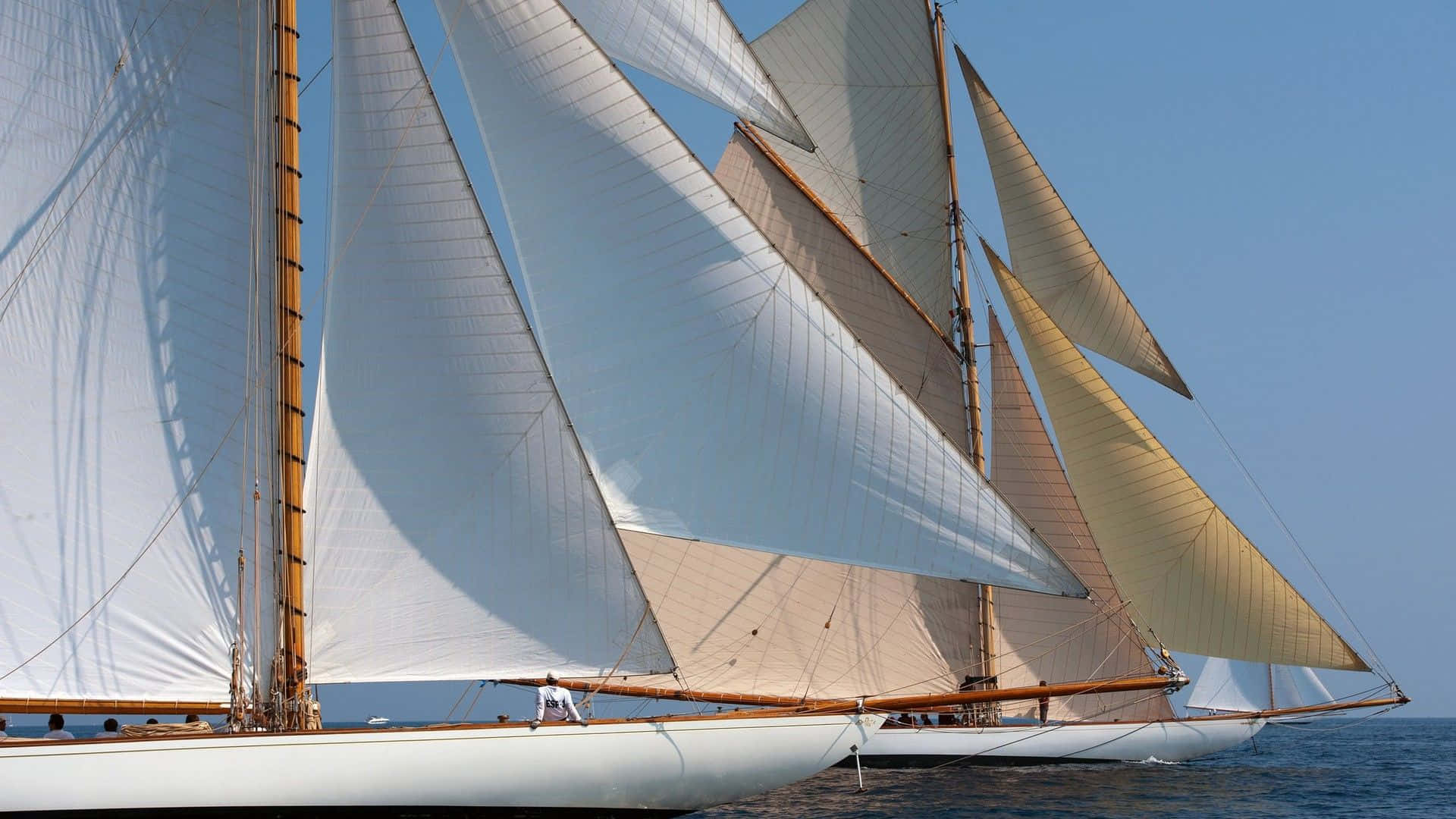 Sailboat 桌布 壁紙 — 經典高桅帆船，白色和棕褐色船帆隨風鼓脹，在晴朗天空下平靜的藍色水面上優雅滑行。