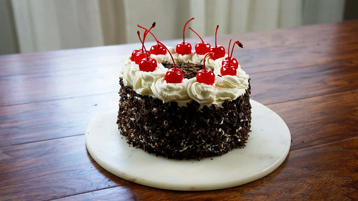 Black Forest Cake 桌布 壁紙 — 經典黑森林蛋糕，上面鋪滿鮮奶油和鮮紅櫻桃，放在木桌上的大理石盤子上。