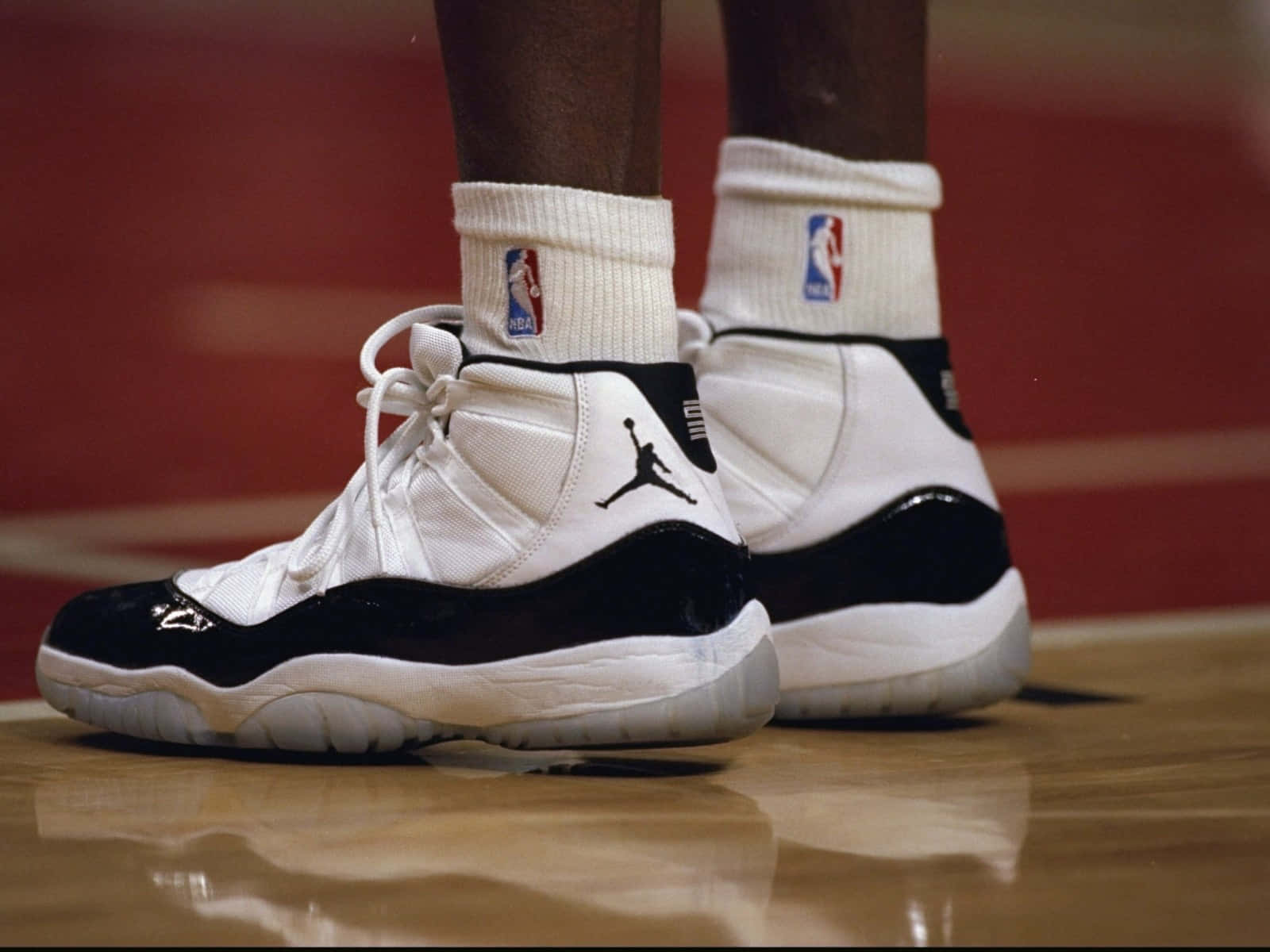 Jordan 桌布 壁紙 — 經典黑白 Air Jordan 11 運動鞋在拋光籃球場上的特寫，搭配NBA襪子。