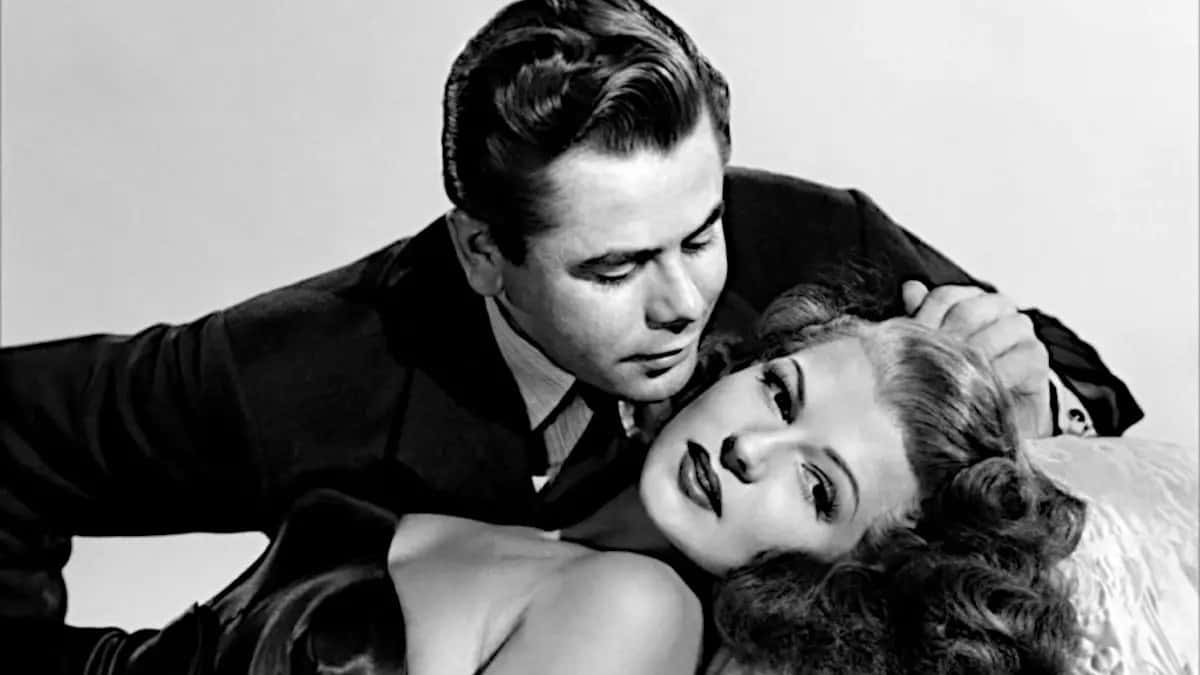 Film Noir 桌布 壁紙 — 經典黑白電影劇照顯示一名身穿西裝的男子俯身靠近一名躺臥的女子，女子妝容誇張，頭髮捲曲。