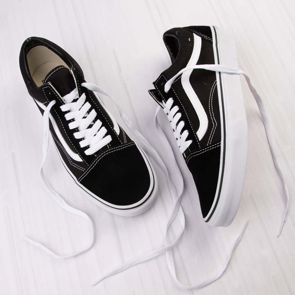 Vans 桌布 壁紙 — 經典黑色Vans Old Skool運動鞋，白色鞋帶和條紋，隨意地放在淺色木地板上。