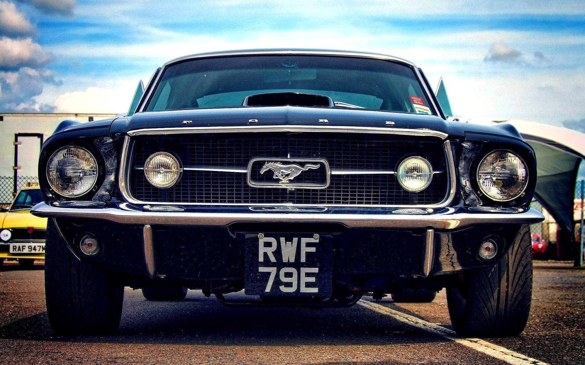 mustang HD 桌布 壁紙 — 經典黑色福特野馬的近距離特寫，帶有鍍鉻細節和馬標誌，背景是明亮的藍天。