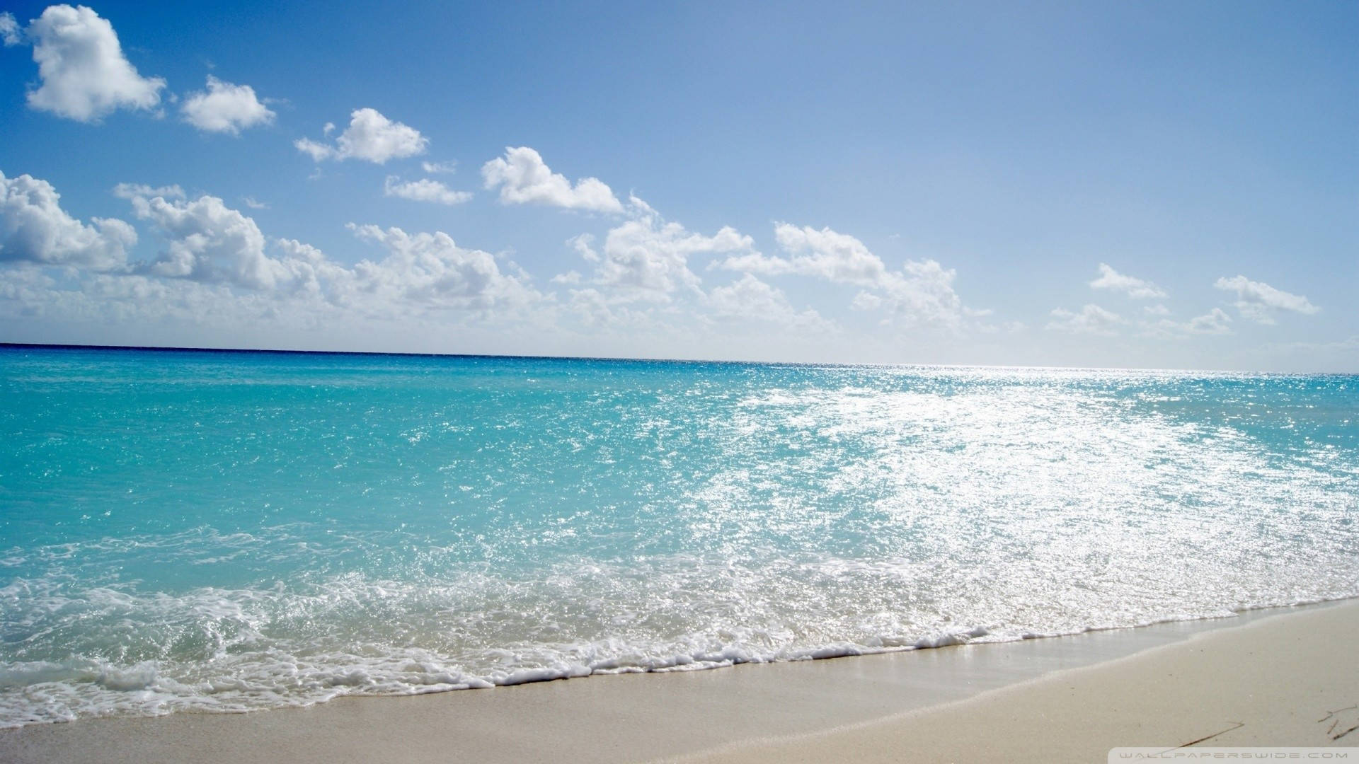 Tropical Beach 桌布 壁紙 — 綠松石色的海浪輕輕拍打在純淨的白色沙灘上，天空湛藍，點綴著蓬鬆的白雲。