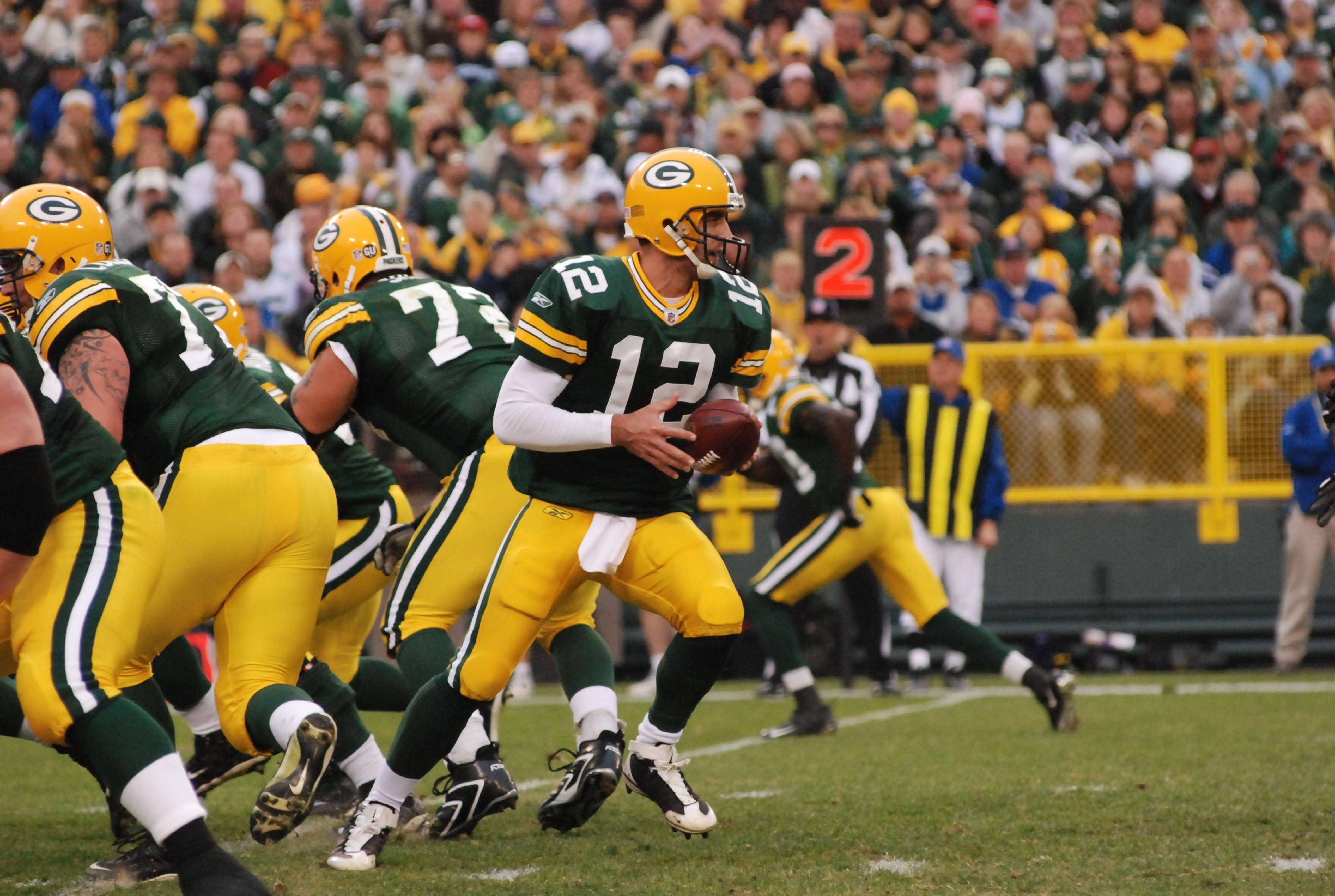 Aaron Rodgers 桌布 壁紙 — 綠灣包裝工四分衛12號身穿綠色和金色制服，在擠滿觀眾的體育場比賽中準備投擲橄欖球。