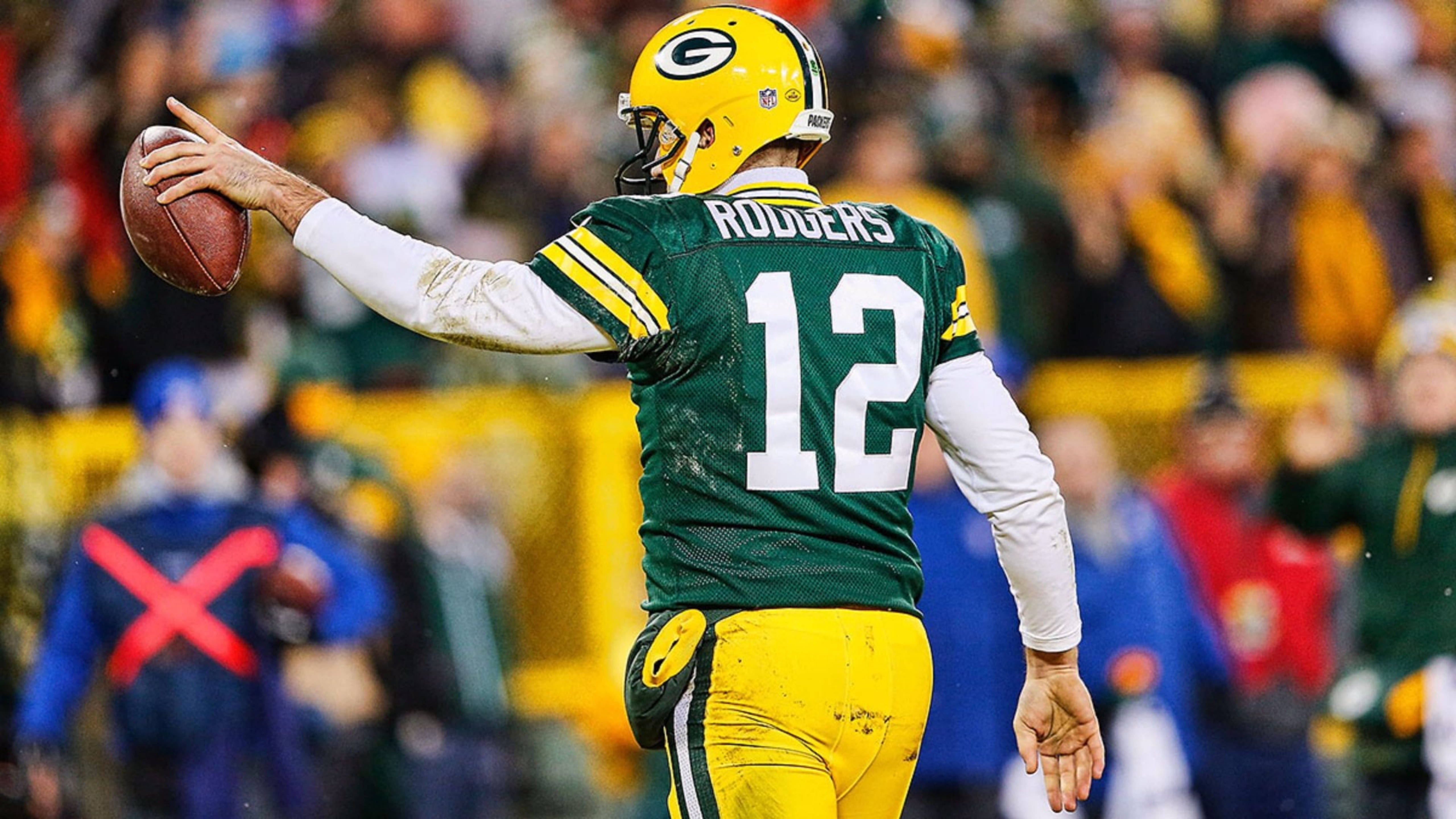 Aaron Rodgers 桌布 壁紙 — 綠灣包裝工四分衛亞倫·羅傑斯身穿綠色和金色制服，在比賽中投擲橄欖球，背景是模糊的體育場人群。