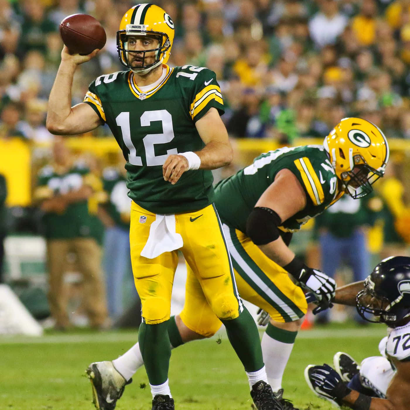 Aaron Rodgers 桌布 壁紙 — 綠灣包裝工的四分衛穿著綠色和金色制服，在夜間比賽中投擲橄欖球，背景是模糊的球迷。