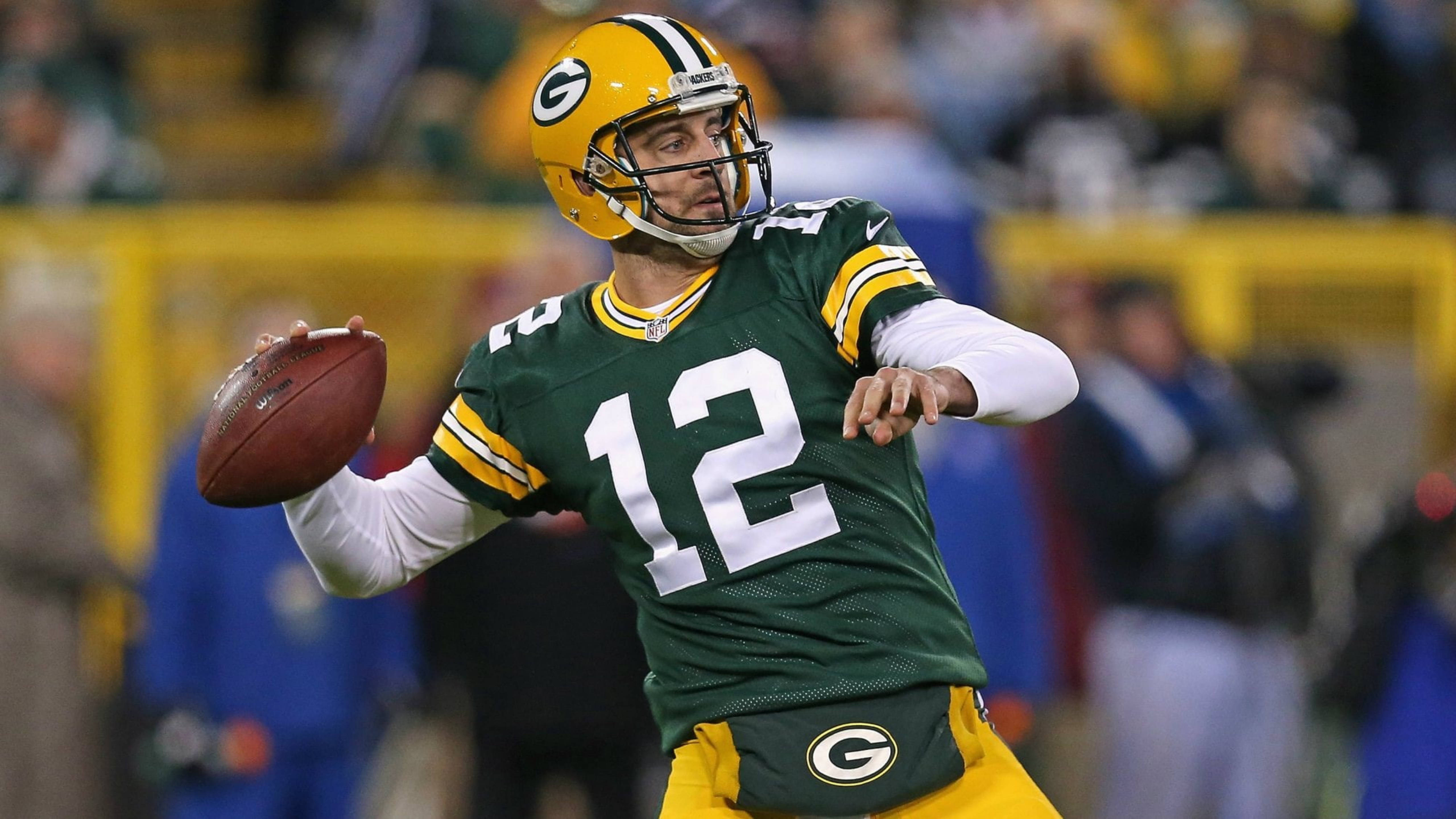 Aaron Rodgers 桌布 壁紙 — 綠灣包裝工的四分衛穿著綠色和金色制服，在夜間比賽中於體育場燈光下投擲橄欖球。