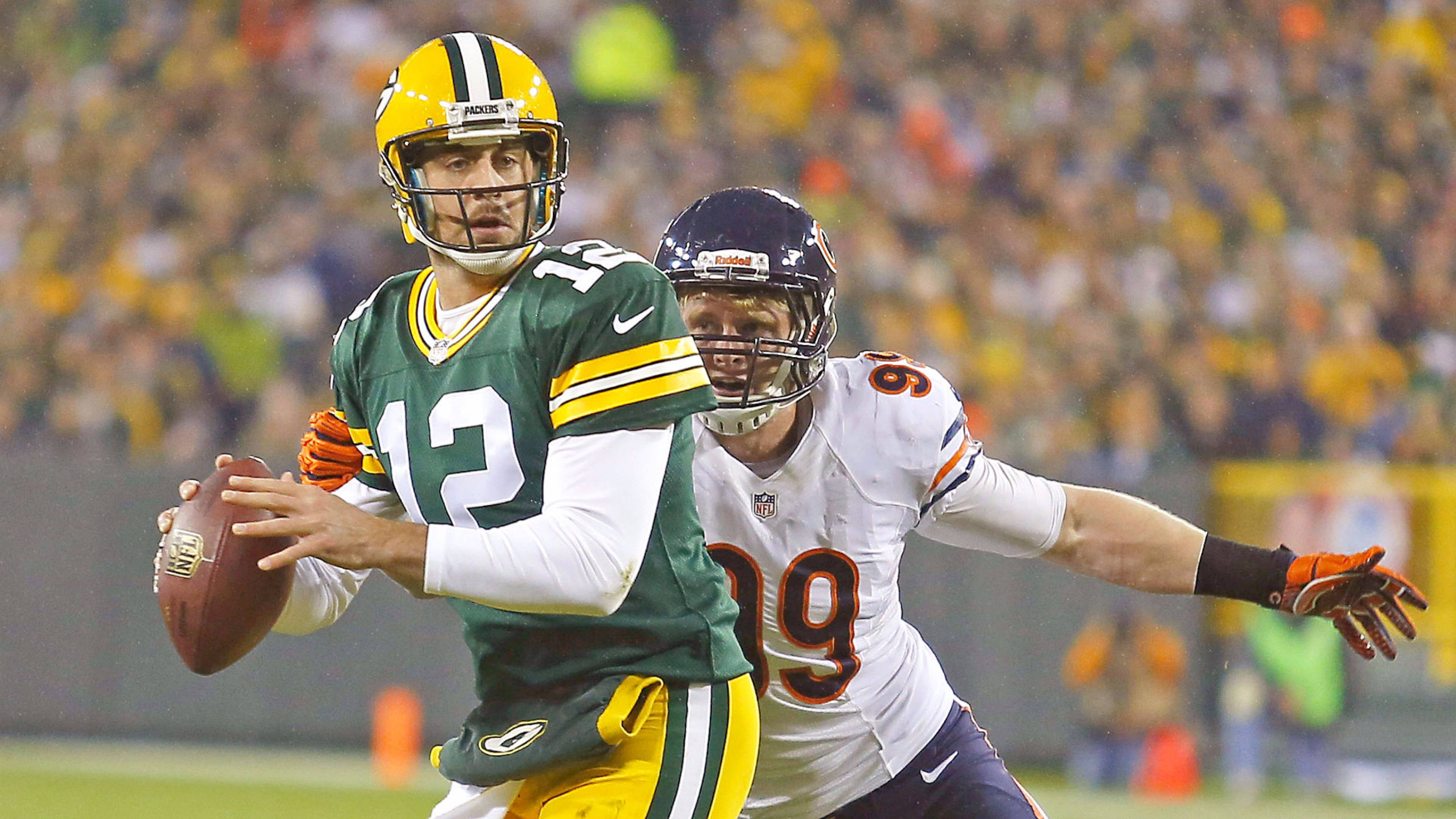 Aaron Rodgers 桌布 壁紙 — 綠灣包裝工的四分衛穿著綠色和黃色制服在夜間比賽中擲出橄欖球，而芝加哥熊隊的防守球員身穿白色球衣逼近。