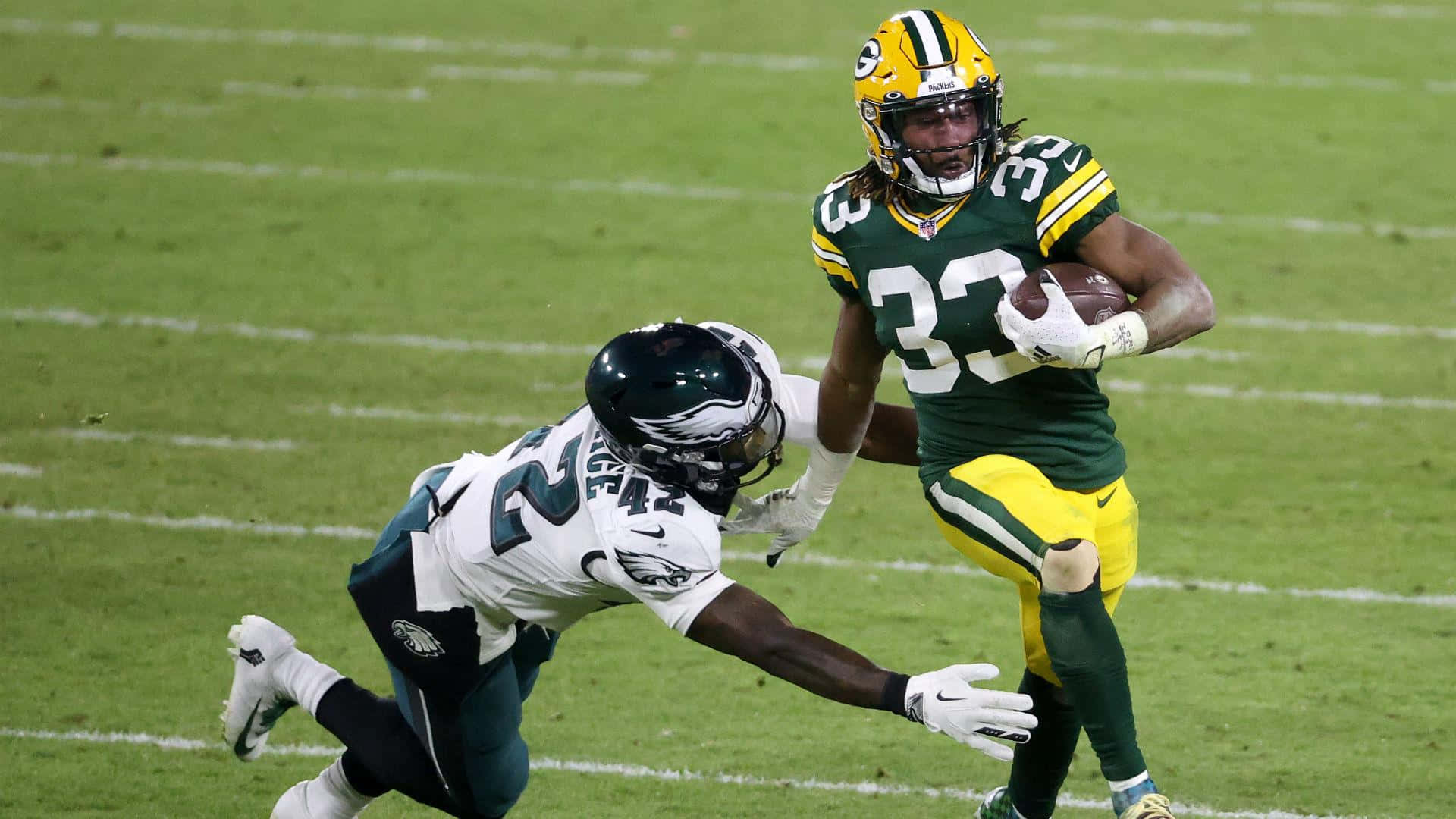 Aaron Jones 桌布 壁紙 — 綠灣包裝工隊32號球員帶著美式足球奔跑，費城老鷹隊防守球員在草地上飛撲試圖擒抱他。