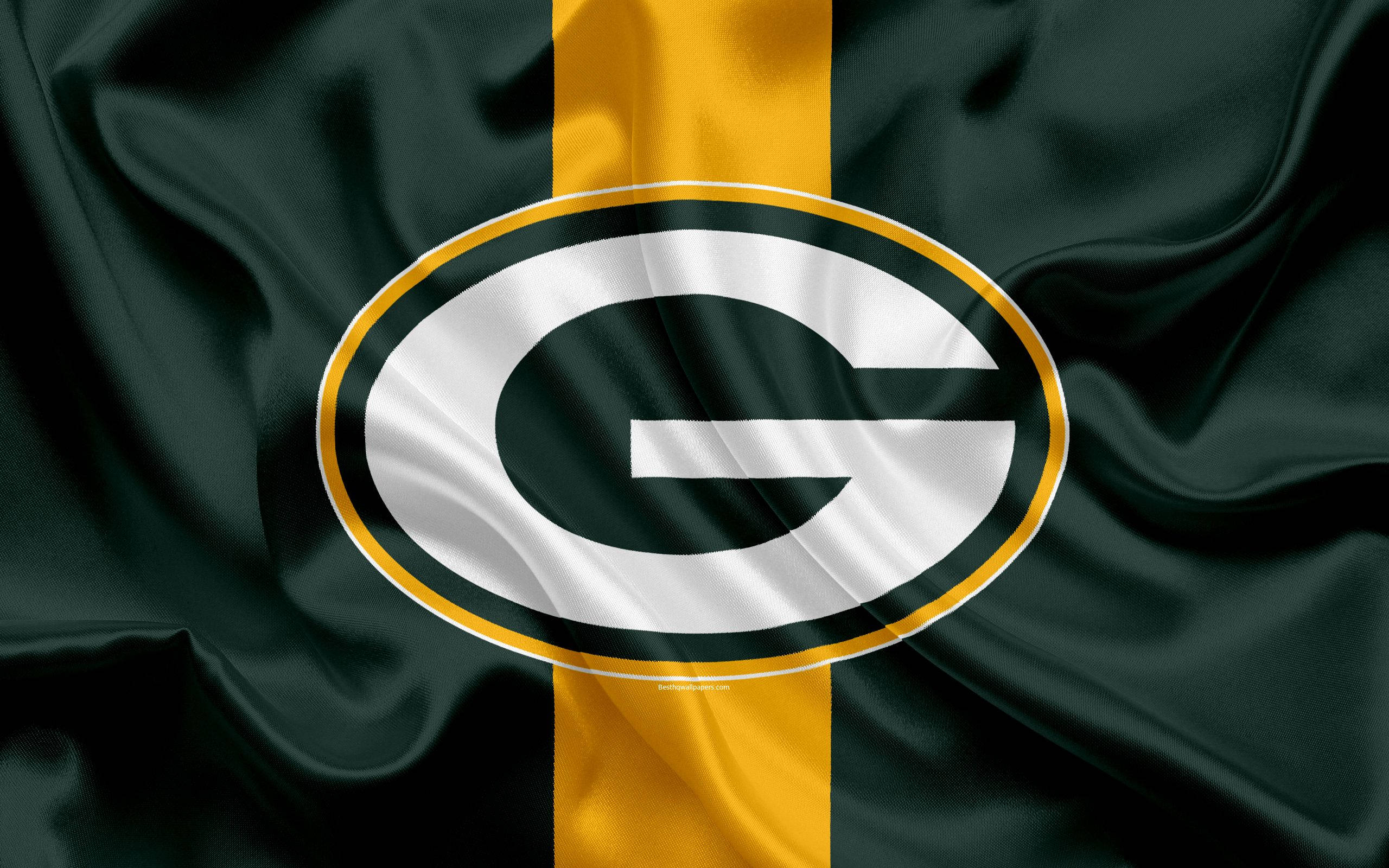 Packers 桌布 壁紙 — 綠灣包裝工隊標誌的特寫，位於深綠色緞面旗幟上，帶有金色條紋和白色橢圓形。