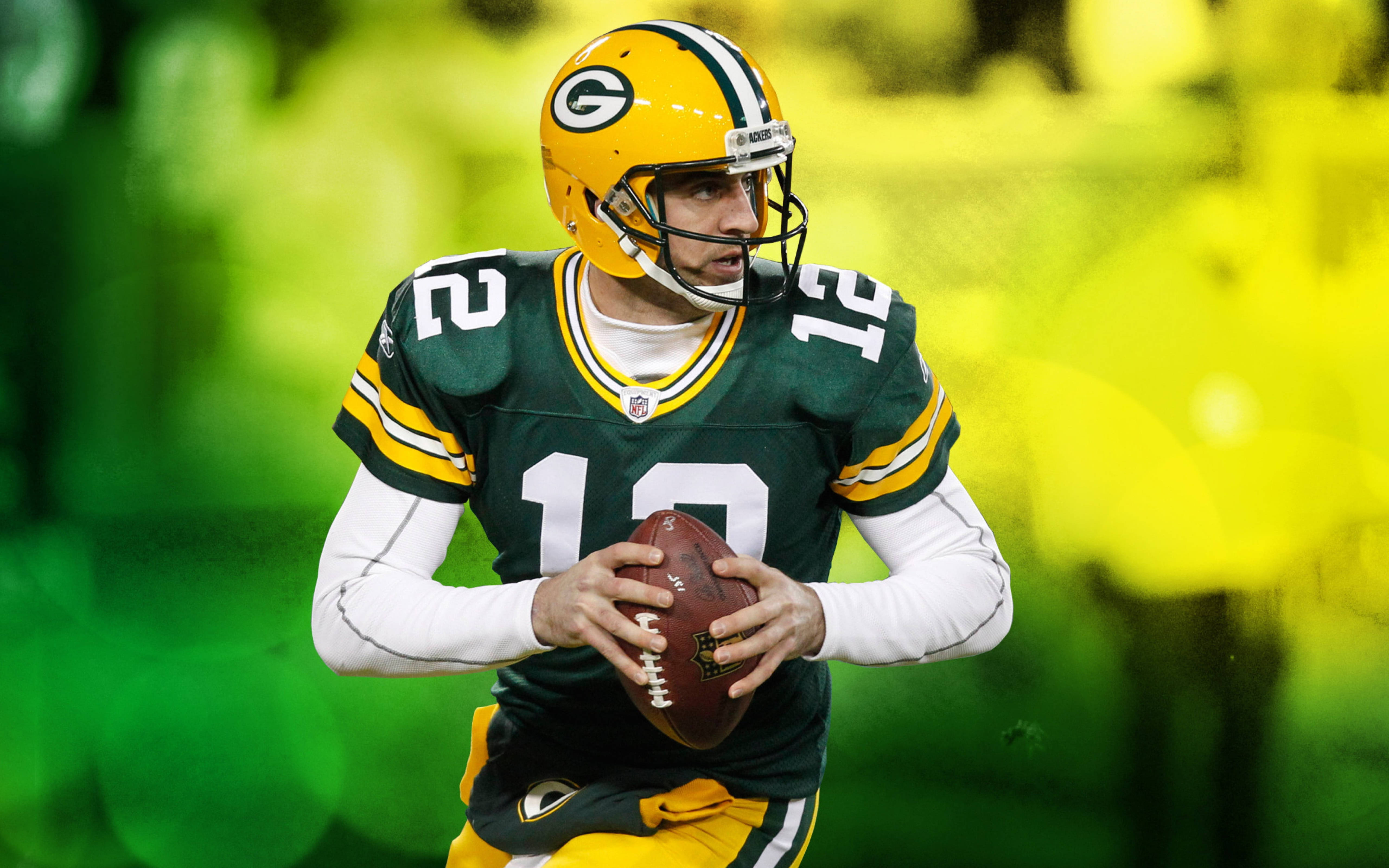 Aaron Rodgers 桌布 壁紙 — 綠灣包裝工隊的四分衛穿著綠色和金色制服，手持橄欖球準備投擲，背景是模糊的體育場。