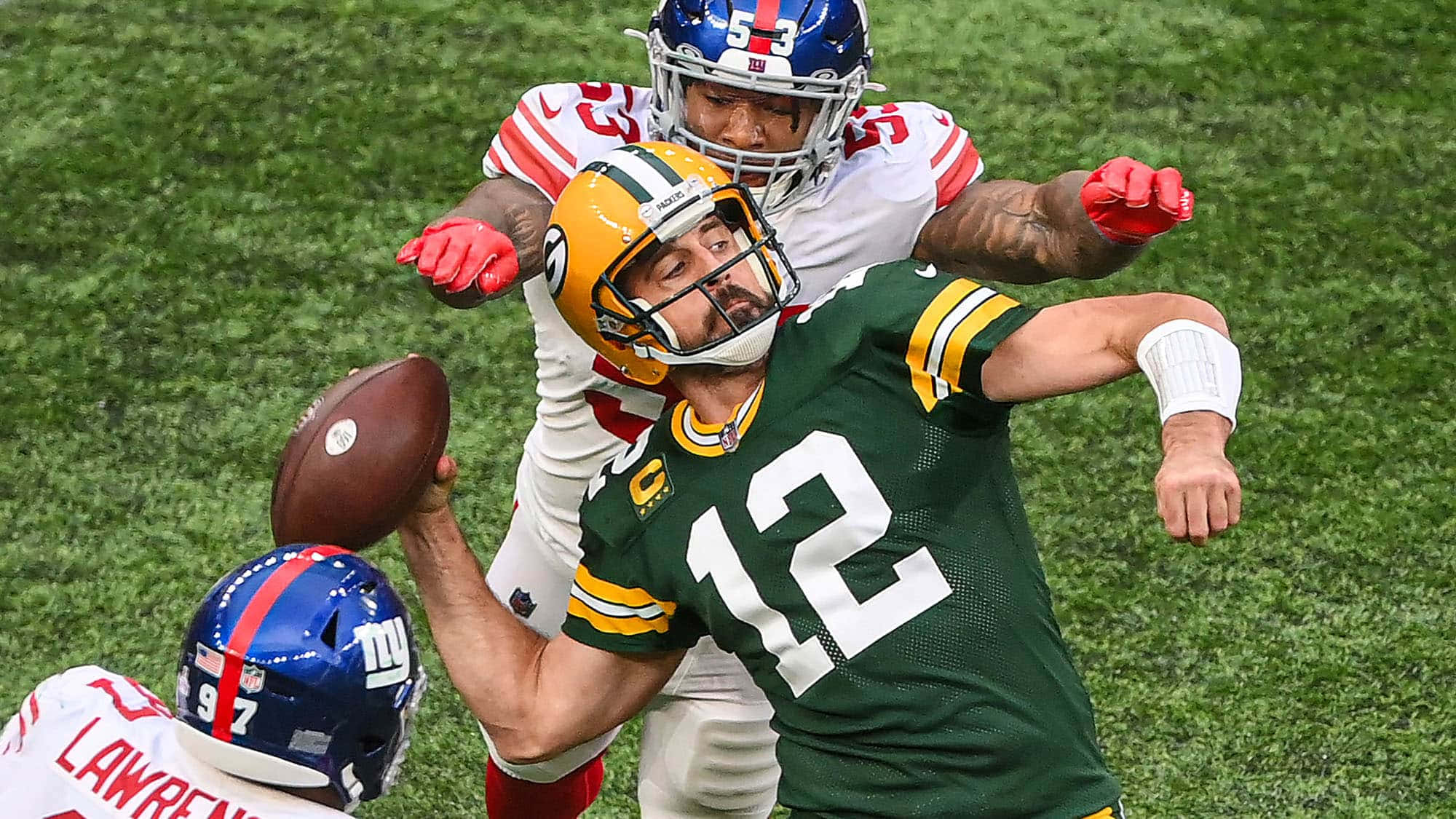 Aaron Rodgers 桌布 壁紙 — 綠灣包裝工隊的四分衛穿著綠色球衣，在充滿活力的綠色球場上被兩名紐約巨人隊的防守球員擒抱時投擲美式足球。