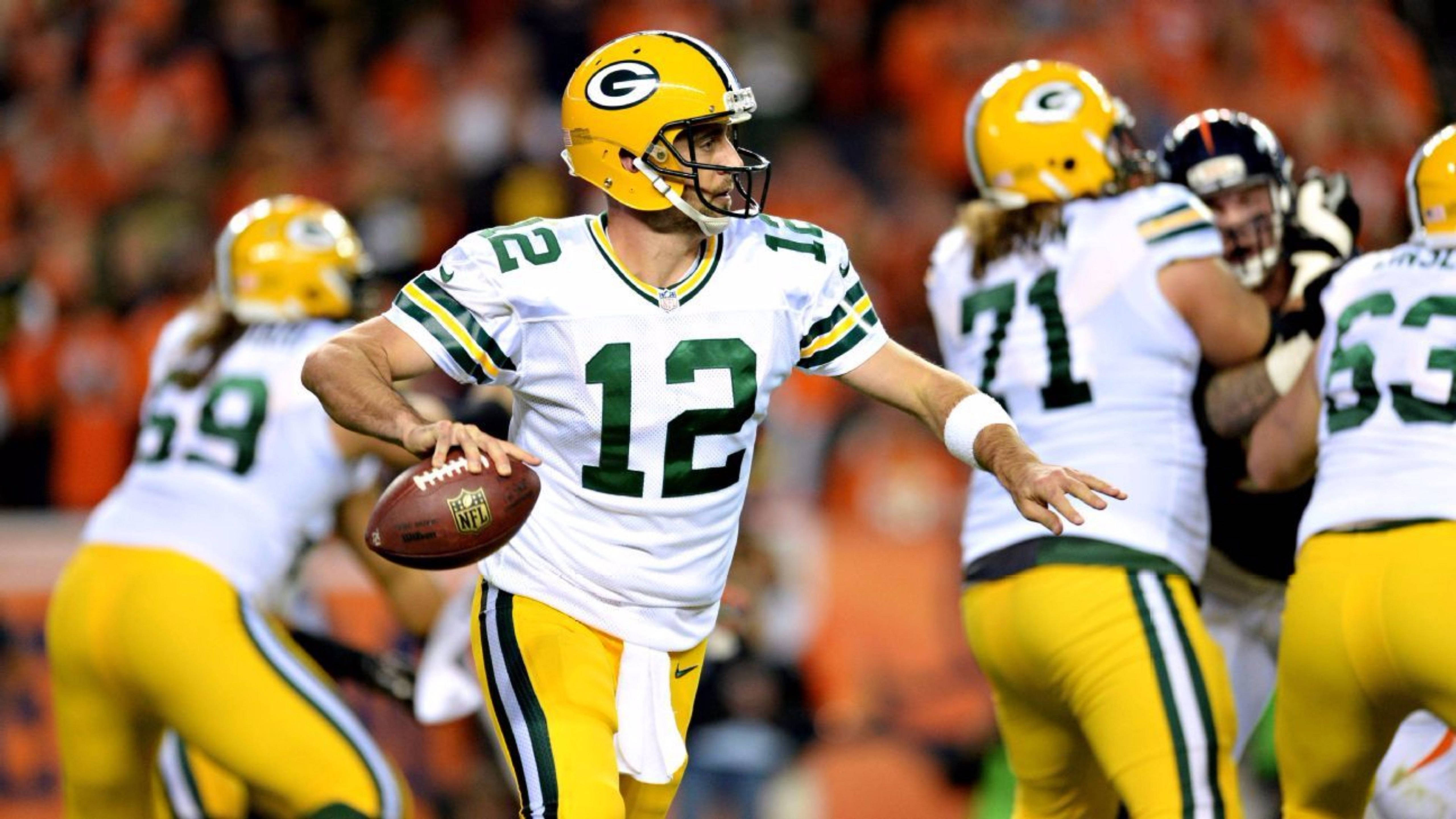 Aaron Rodgers 桌布 壁紙 — 綠灣包裝工隊的四分衛身穿白色和黃色球衣，在夜間比賽中準備傳球。