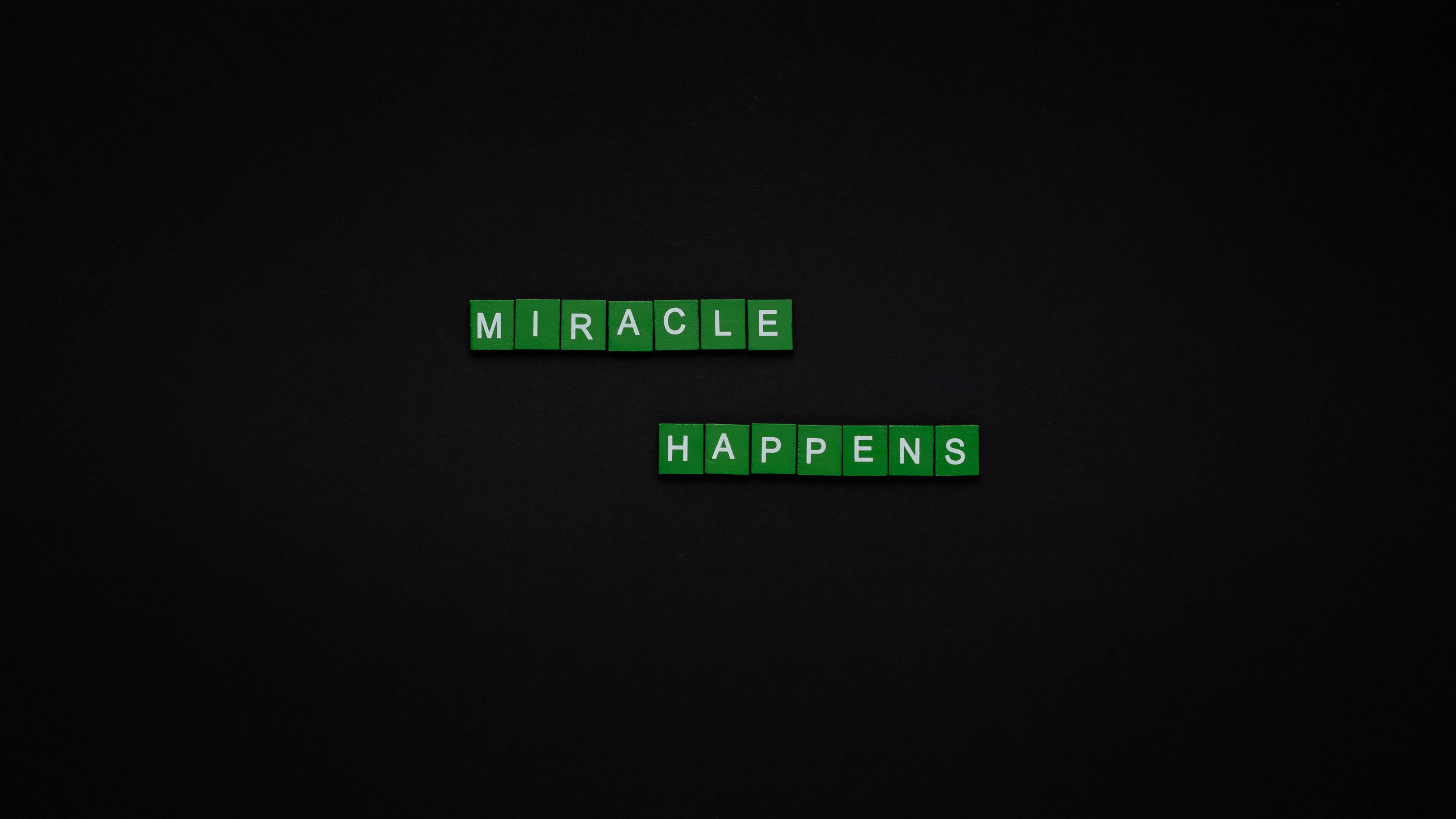 Screen 桌布 壁紙 — 綠色 Scrabble 字母磚在深色紋理背景中央拼出 miracle happens。
