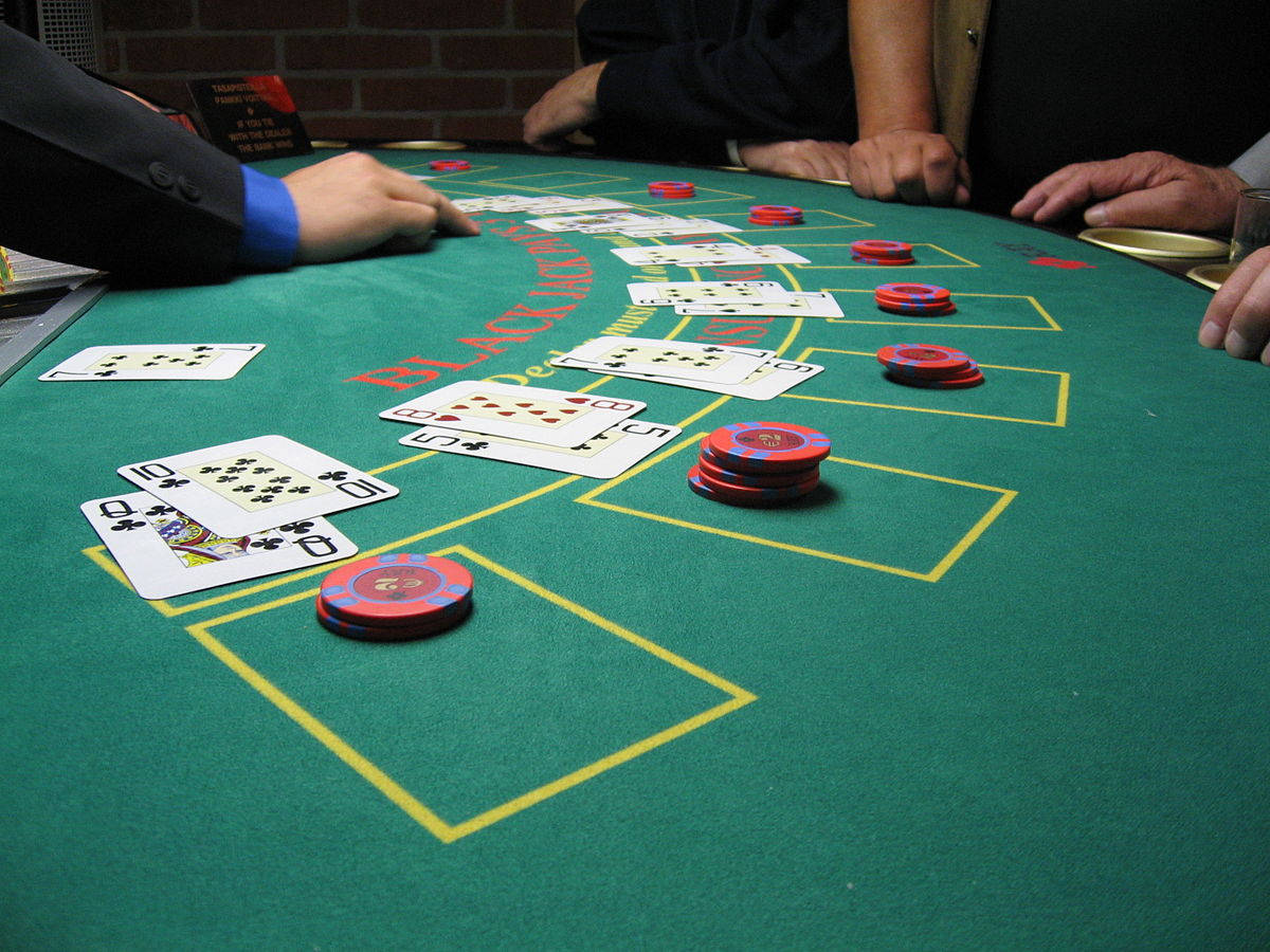 Casino 桌布 壁紙 — 綠色二十一點桌的特寫，散落的撲克牌和紅色籌碼，玩家的手在投注區上方懸浮。