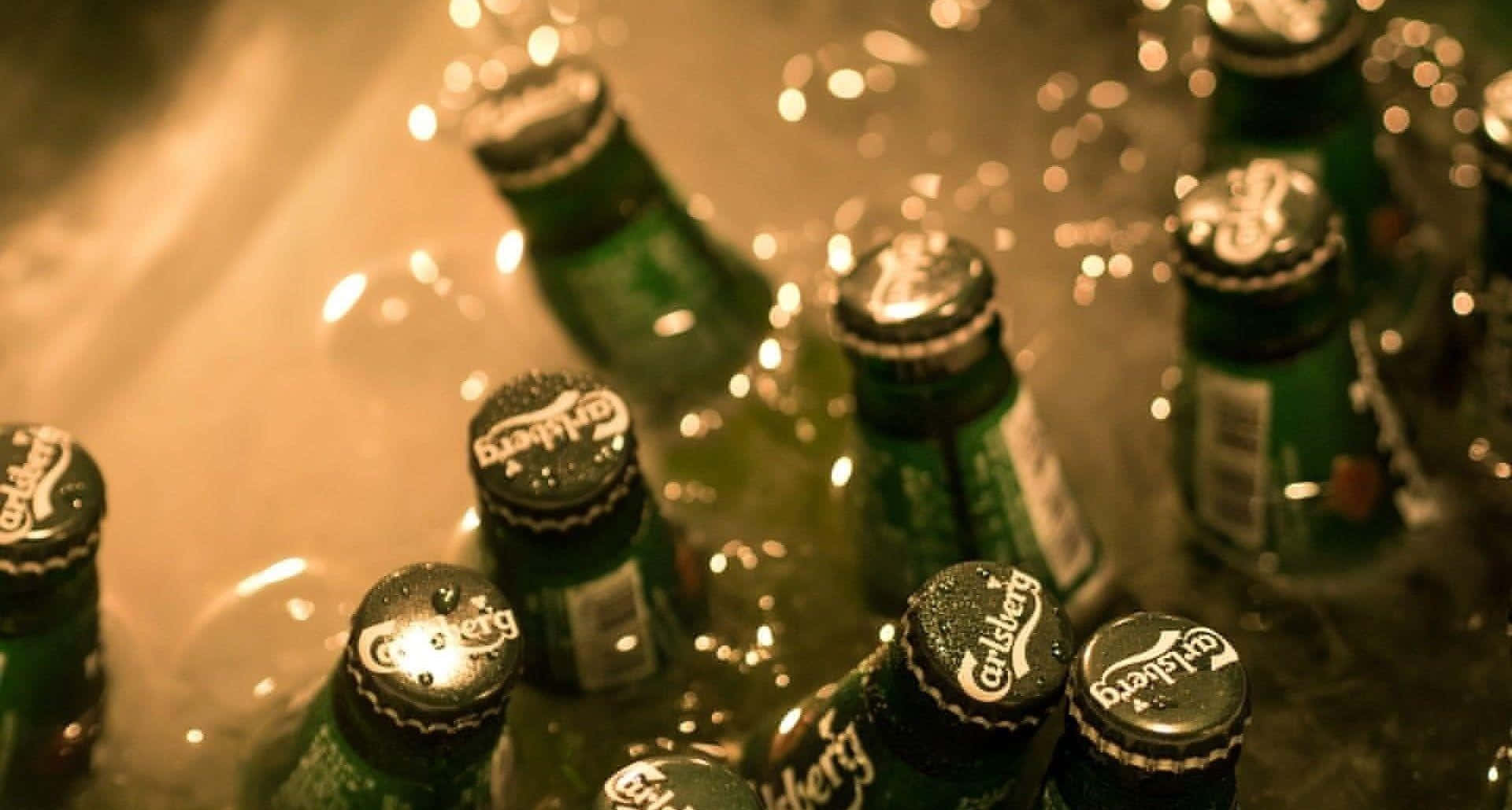 alcohol 桌布 壁紙 — 綠色嘉士伯啤酒瓶在冰中冷藏，帶有溫暖的金色燈光和閃閃發光的冷凝水珠。