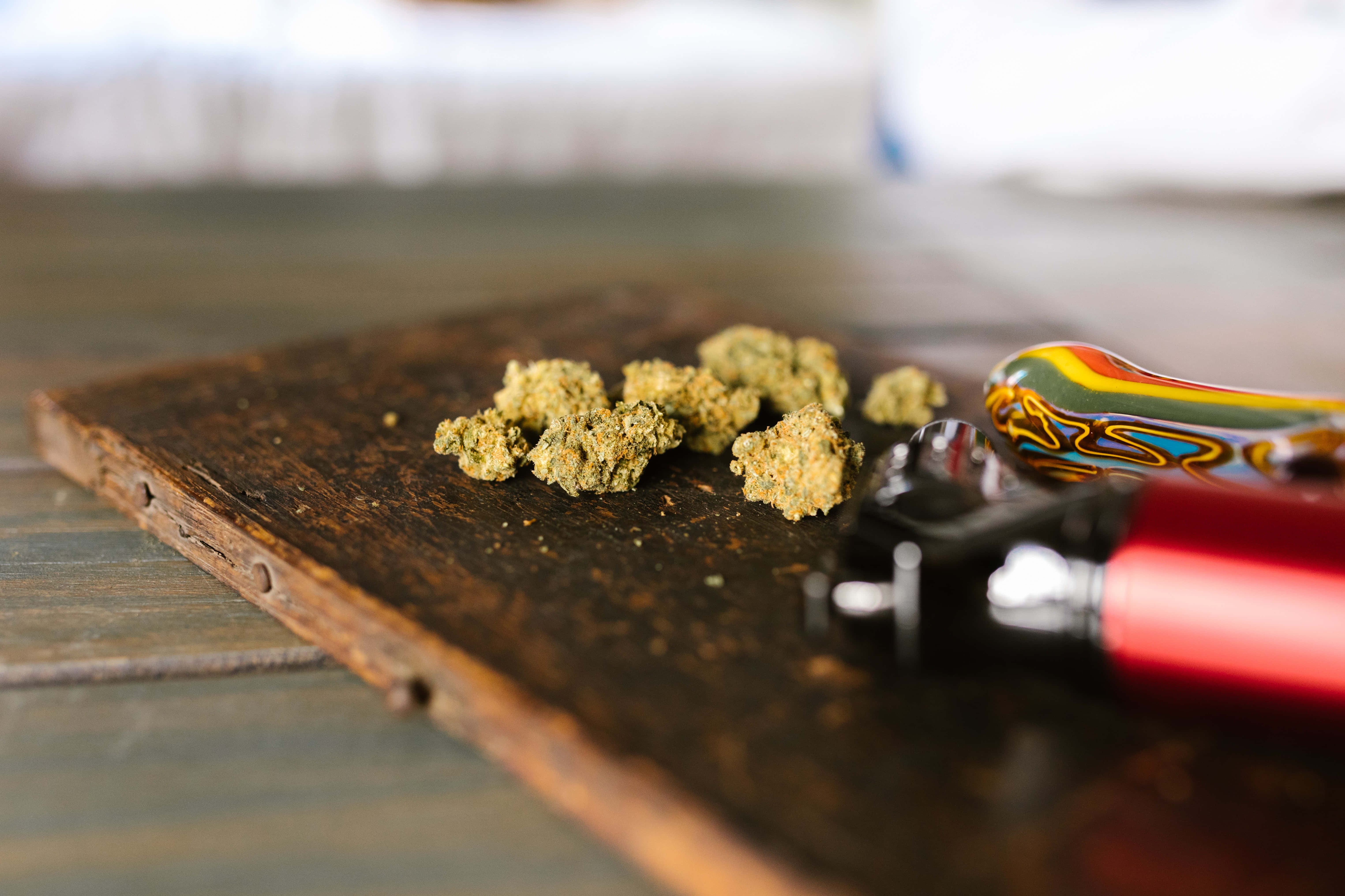 Weed Blunt 桌布 壁紙 — 綠色大麻花蕾和彩色煙斗的特寫，放在一塊風化的木板上。