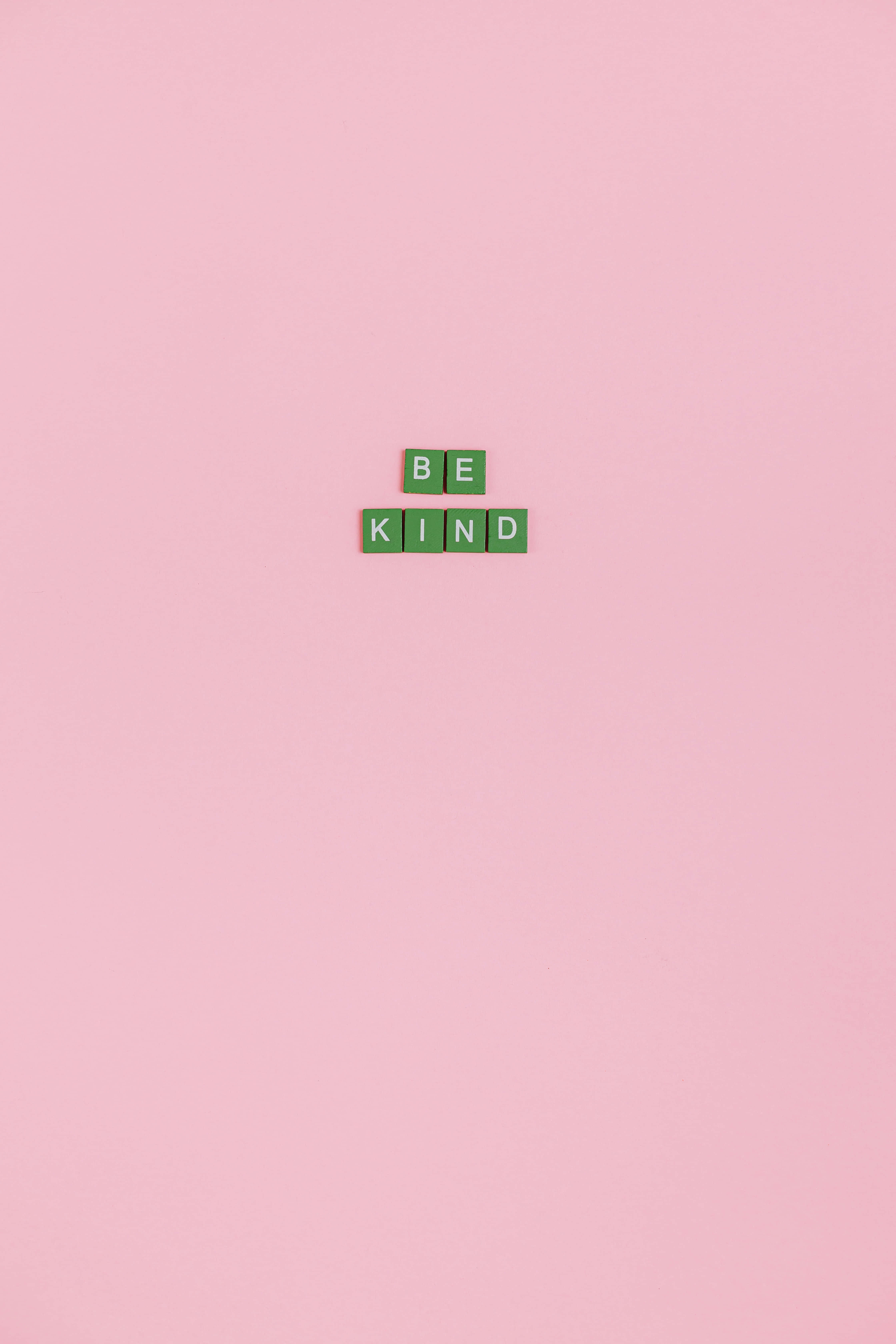 Be Kind 桌布 壁紙 — 綠色字母拼字磚在柔和的粉紅色極簡背景中央拼出「BE KIND」。