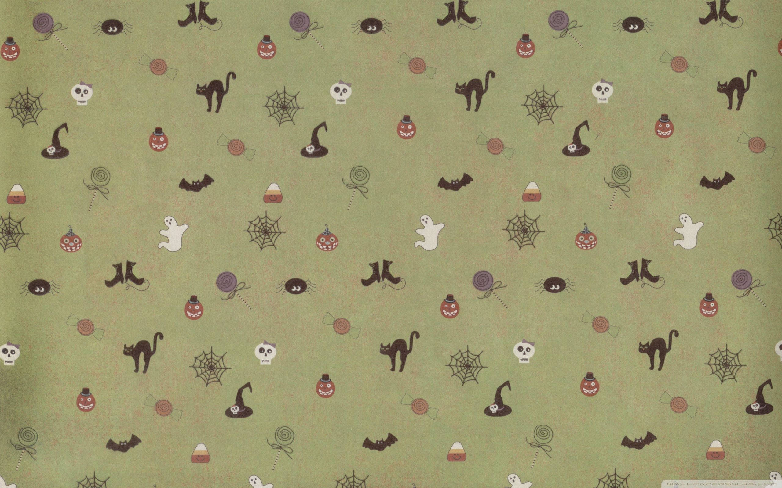 Cute Aesthetic Halloween 桌布 壁紙 — 綠色布料上印有萬聖節圖案，如黑貓、鬼魂、蜘蛛和糖果玉米，呈現俏皮散落的設計。