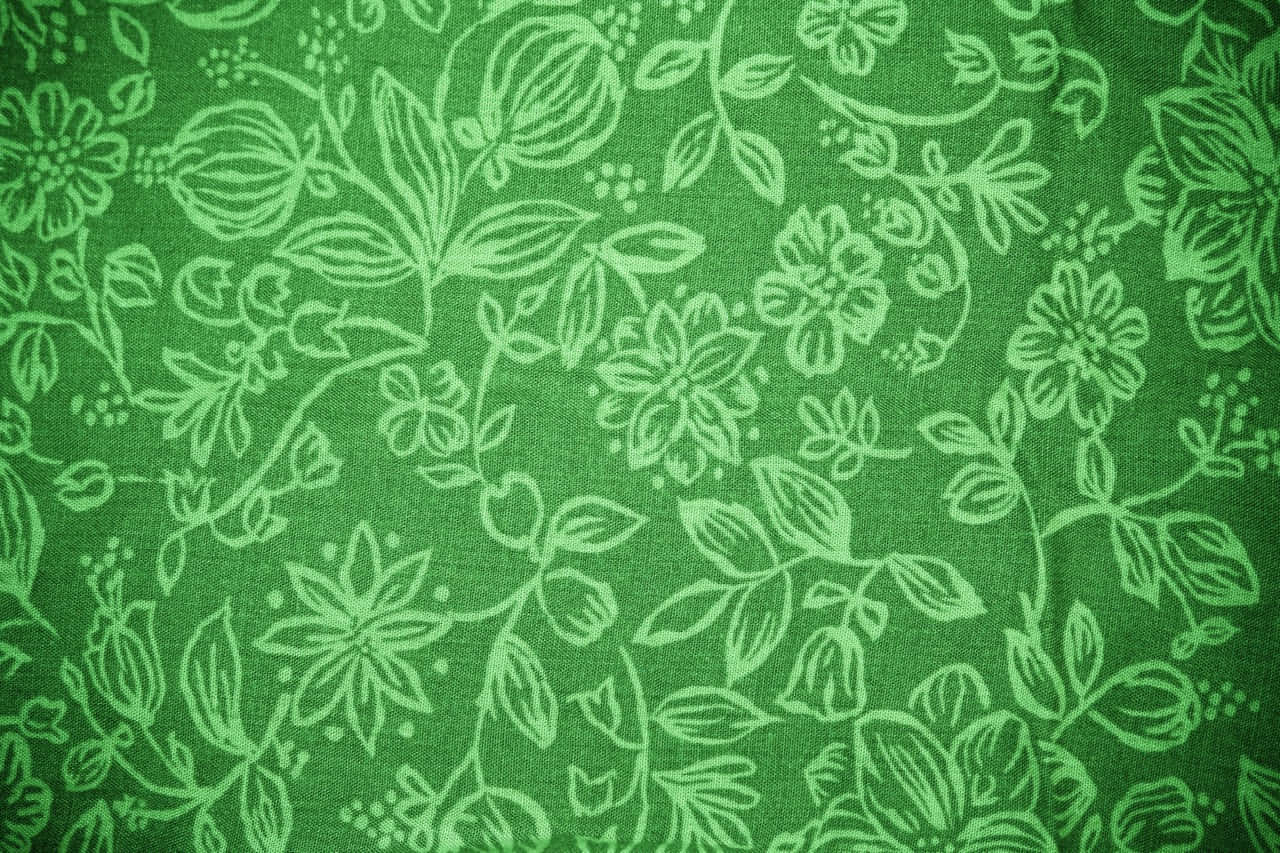 Green Floral 桌布 壁紙 — 綠色布料的特寫，帶有精緻的白色花卉圖案和可見的編織紋理。