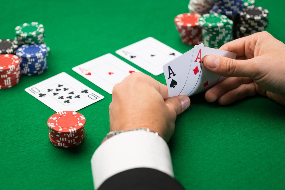 Playing Cards 桌布 壁紙 — 綠色撲克牌桌上，雙手持有兩張Ace，周圍有彩色籌碼和翻開的撲克牌的特寫。