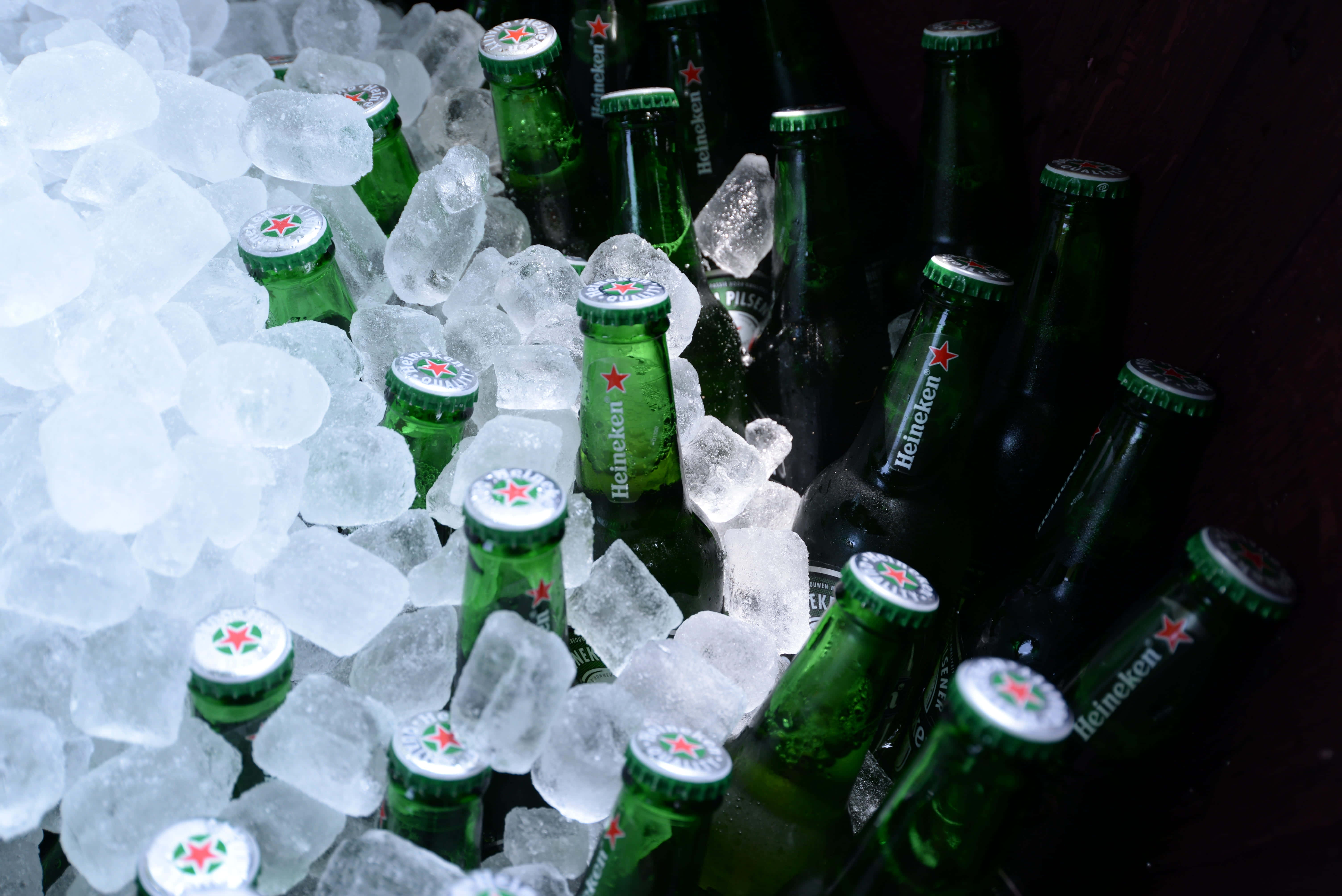 酷 桌布 壁紙 — 綠色海尼根啤酒瓶在戲劇性燈光下，依偎在閃閃發光的冰塊中。
