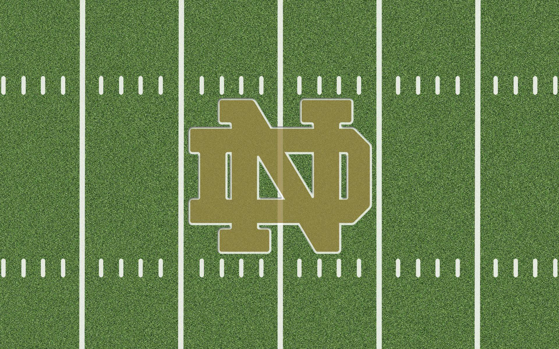 Notre Dame Football 桌布 壁紙 — 綠色足球場的鳥瞰圖，帶有白色碼線和中央的金色聖母大學標誌。