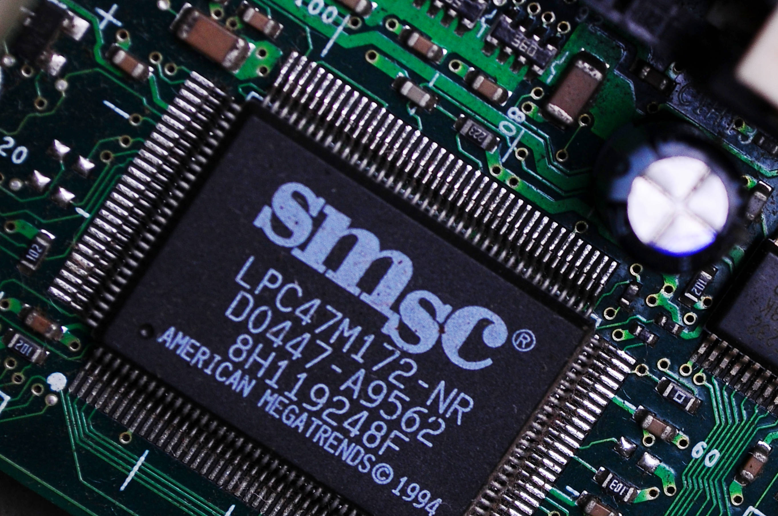 Motherboard 桌布 壁紙 — 綠色電路板特寫，帶有SMSC晶片、可見的焊點和元件標記。
