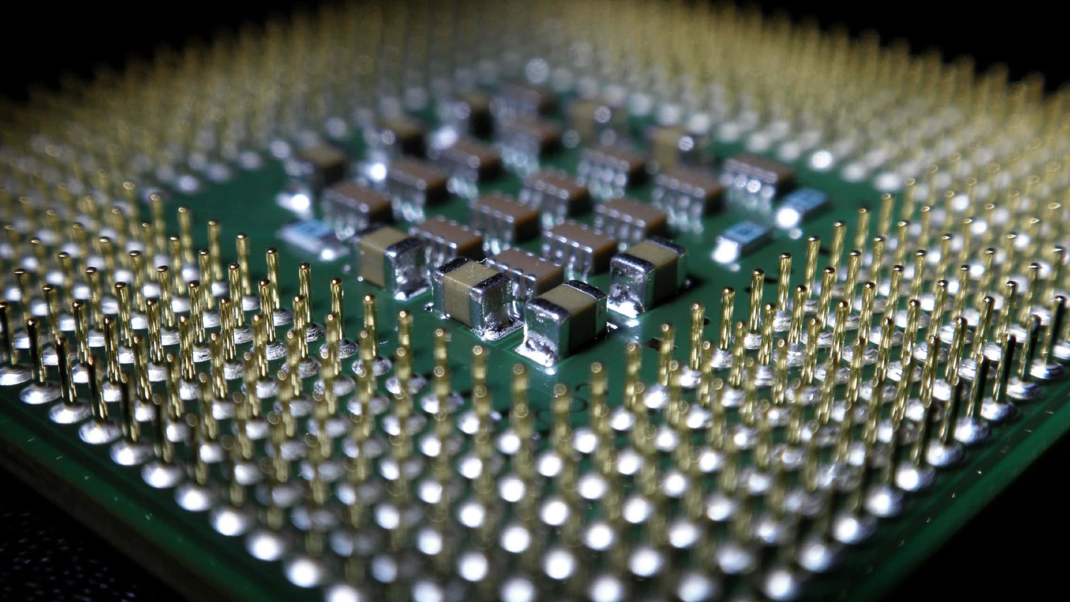 4K Processor 桌布 壁紙 — 綠色電路板特寫，帶有金色引腳和閃亮金屬元件，在明亮燈光下。