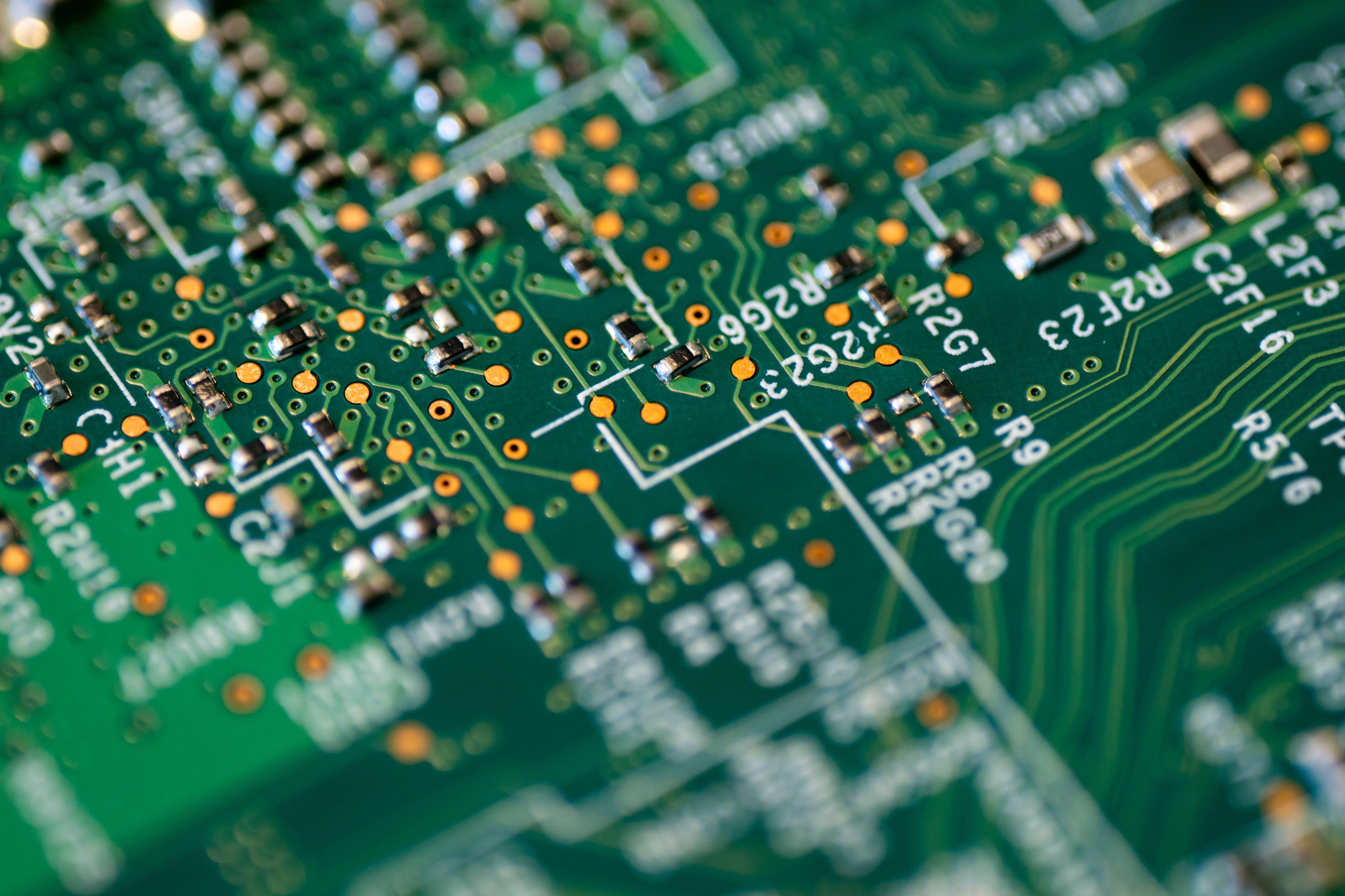 Motherboard 桌布 壁紙 — 綠色電路板的微距照片，帶有複雜的銀色路徑和細小的橙色焊點。