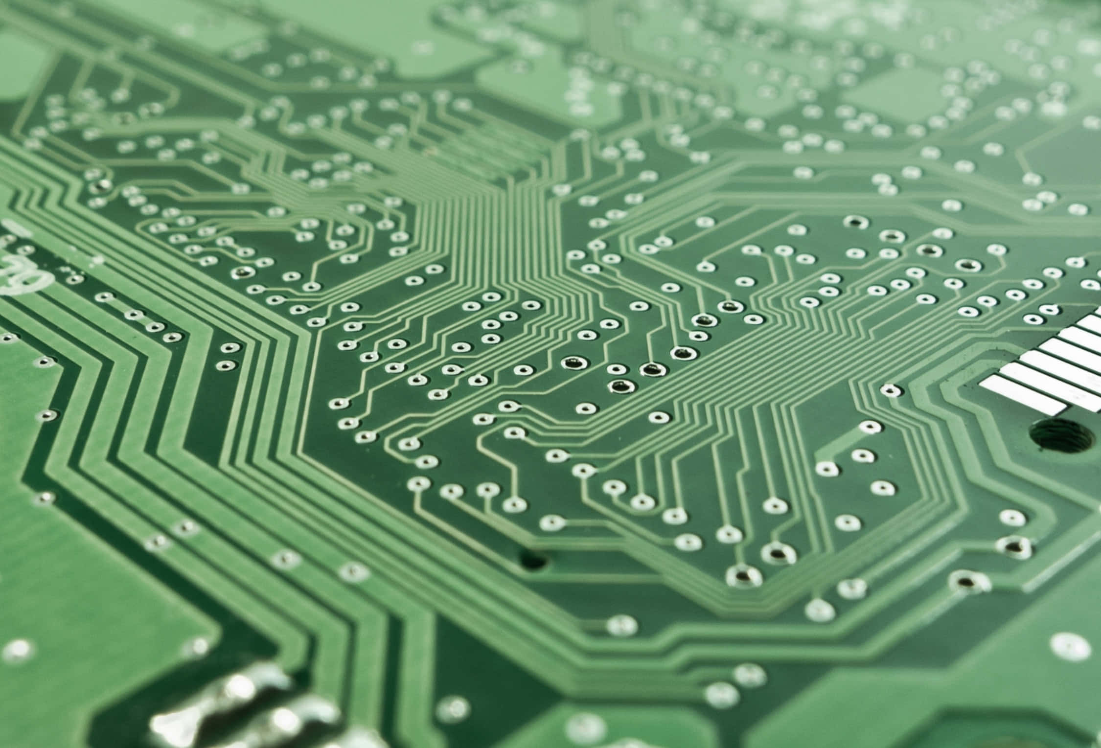 Motherboard 桌布 壁紙 — 綠色電路板的特寫，帶有複雜的銀色線路和焊點，在柔和光線下。